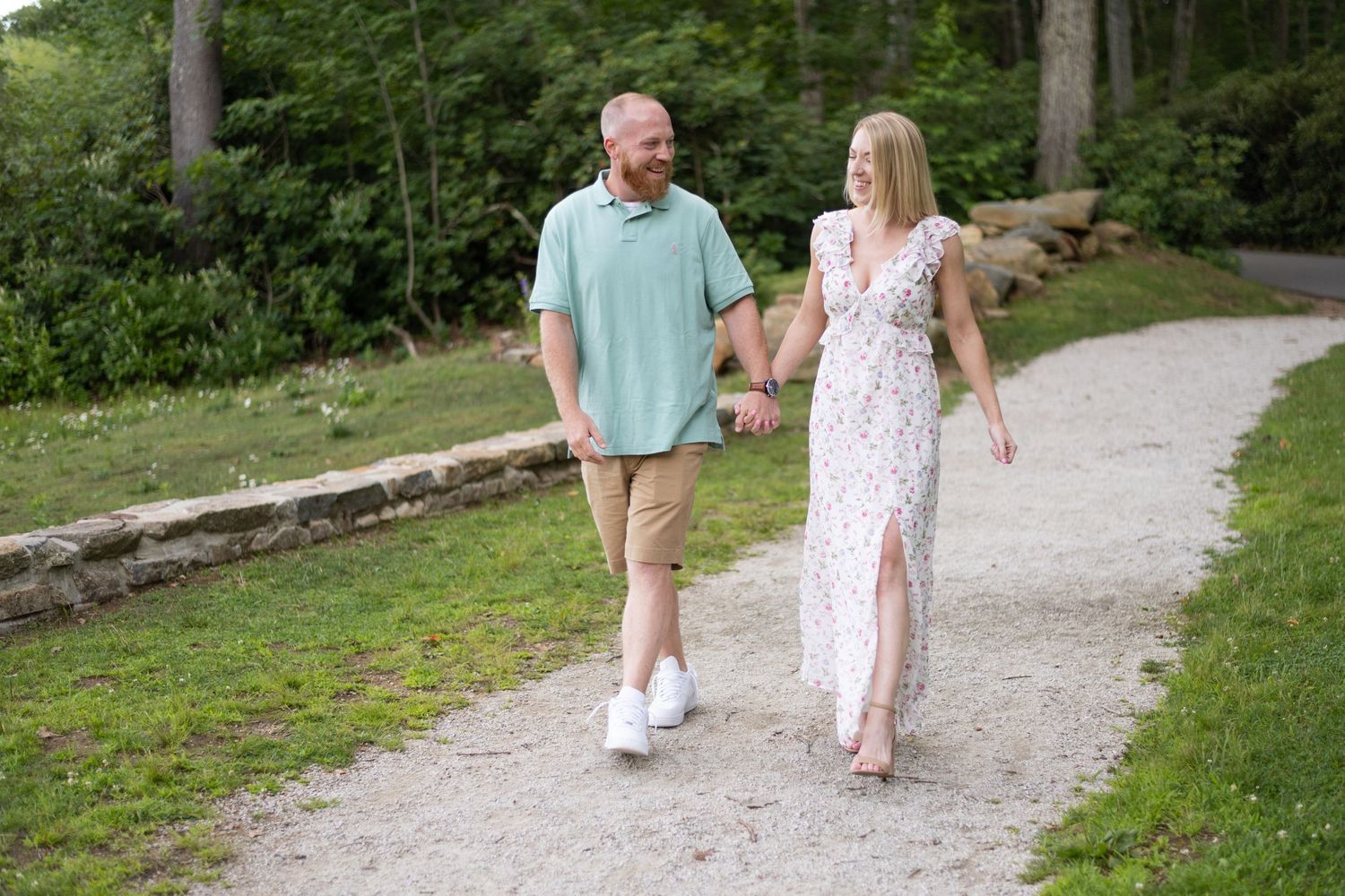 Couple walking hand in hand along a scenic wooded path in casual summer attire.