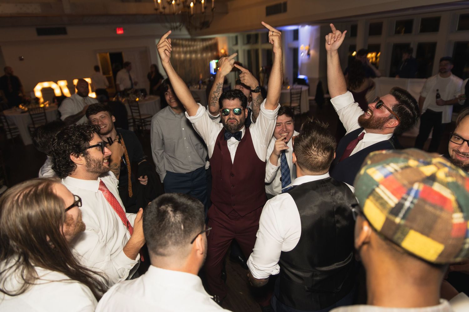 Crowded dance floor at a party with people dancing and raising their hands in a dimly lit room.