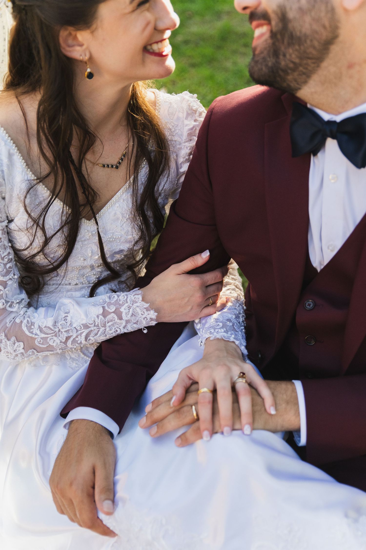 A couple in wedding attire share a joyful moment together outdoors with the bride wearing a white lace dress.