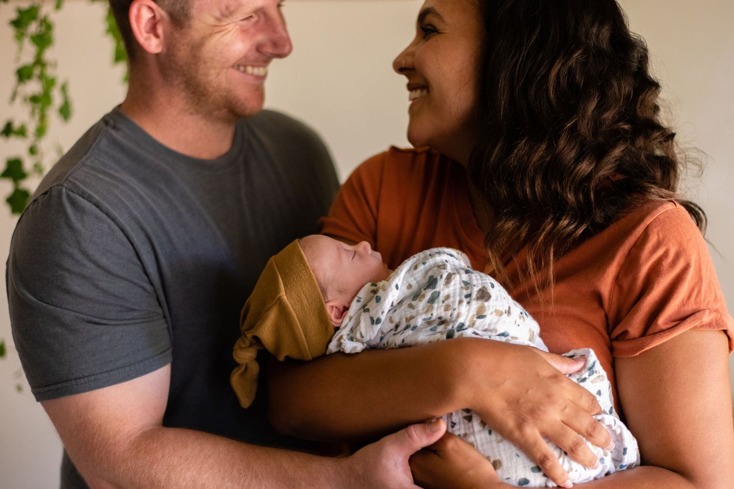 Family sharing intimate moments with newborn baby indoors near window with plants.