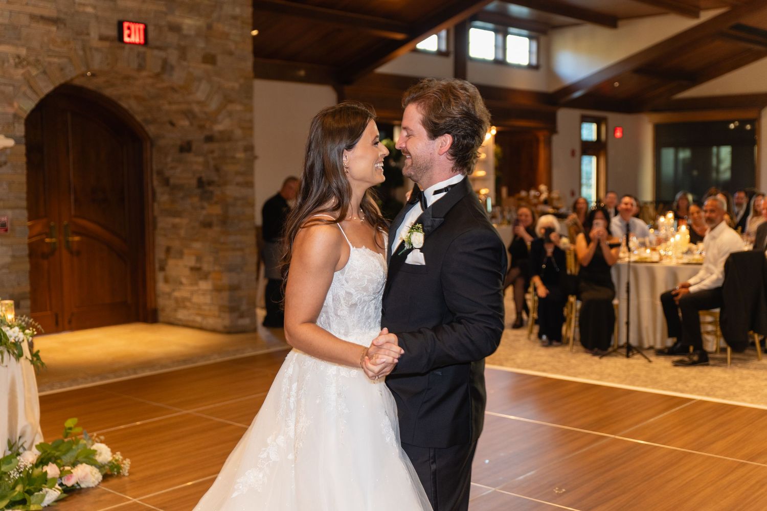 A couple shares their first dance at a rustic venue with exposed brick walls and wooden beams.