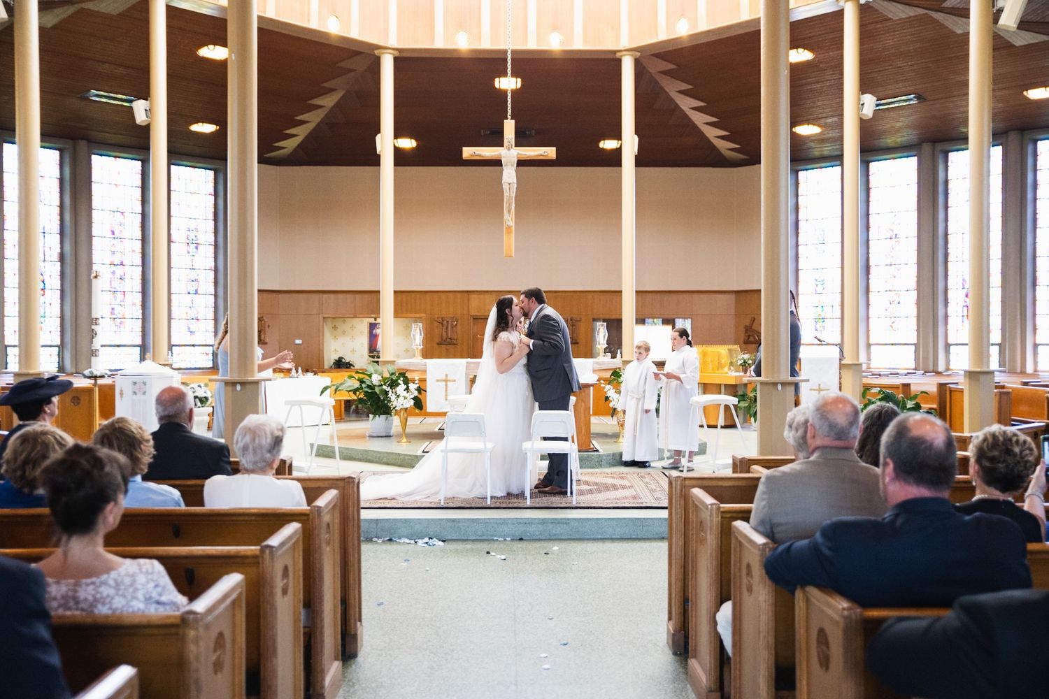 Wedding ceremony in modern church with large windows and wooden cross at altar.