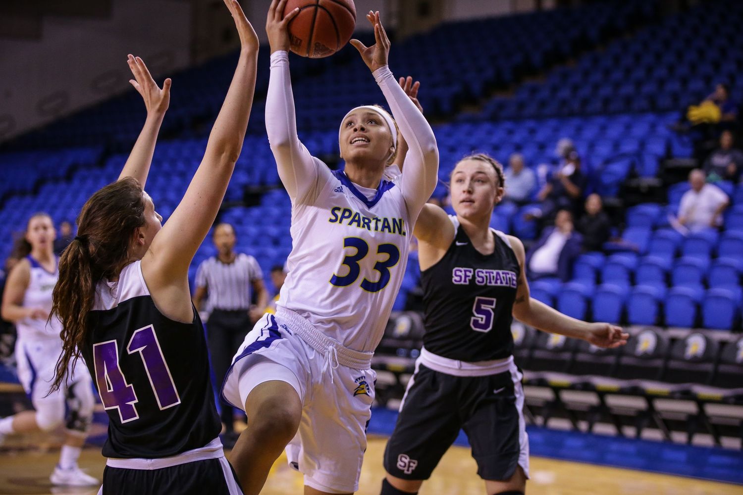 Spartans #33 drives to basket against defenders in womens college basketball game.