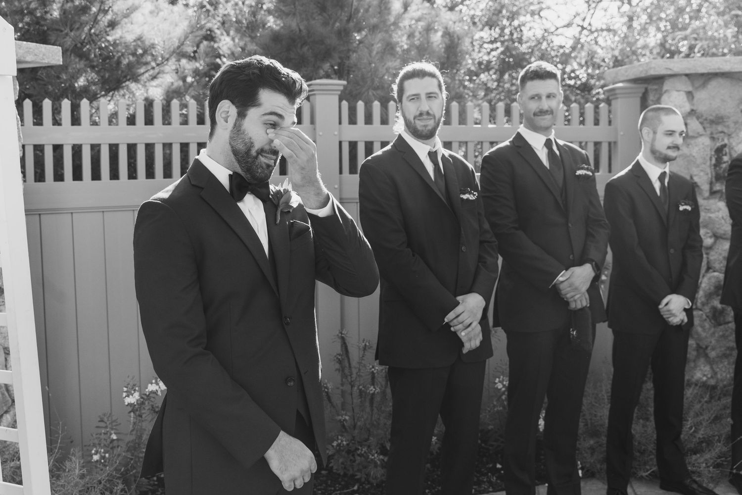 Black and white photo of groomsmen lined up outdoors for formal wedding portraits.