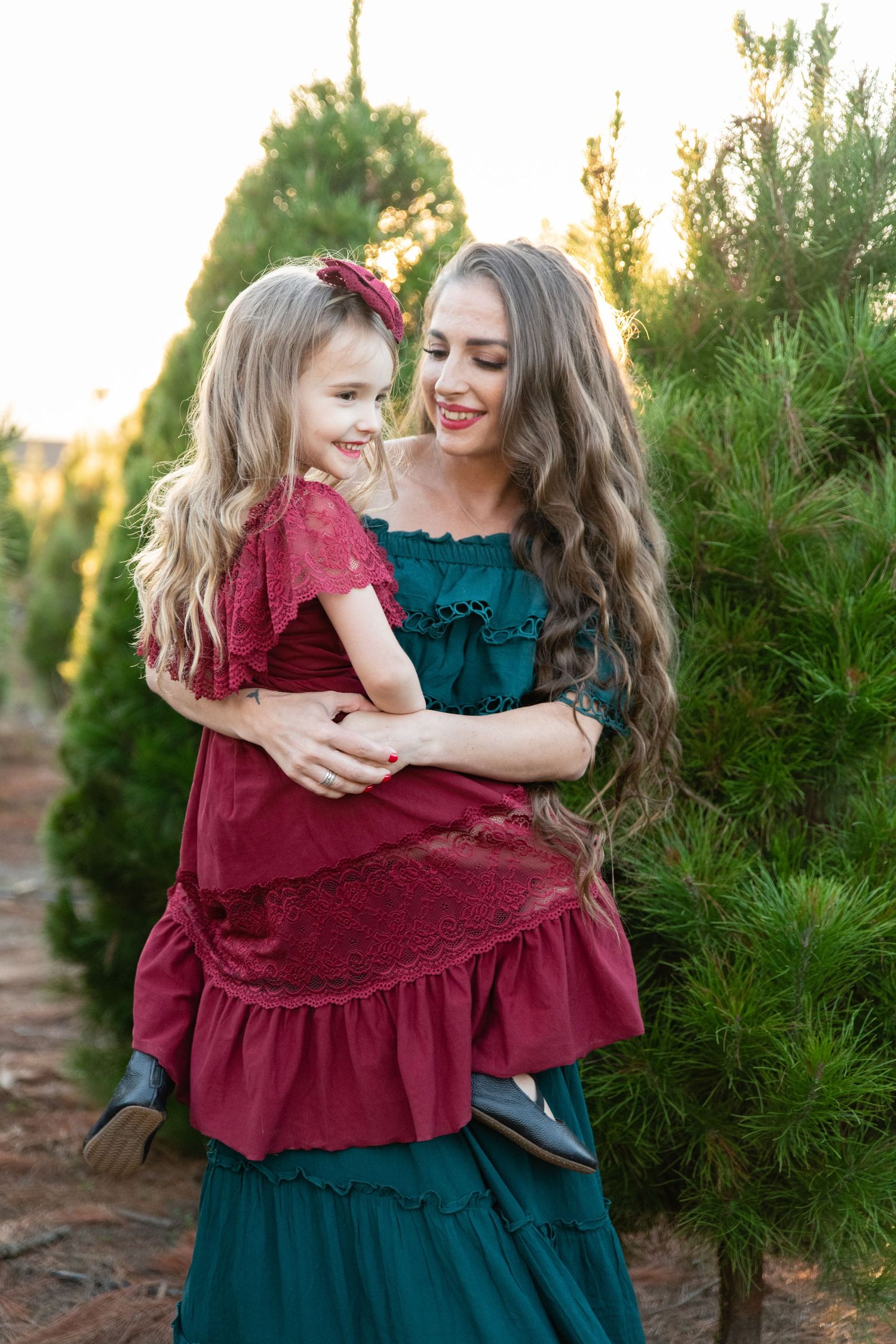 Two people share tender moments among evergreen trees at sunset.