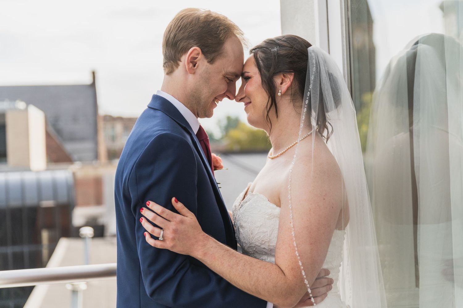 A bride and groom share an intimate moment during their wedding ceremony against a bright window backdrop.