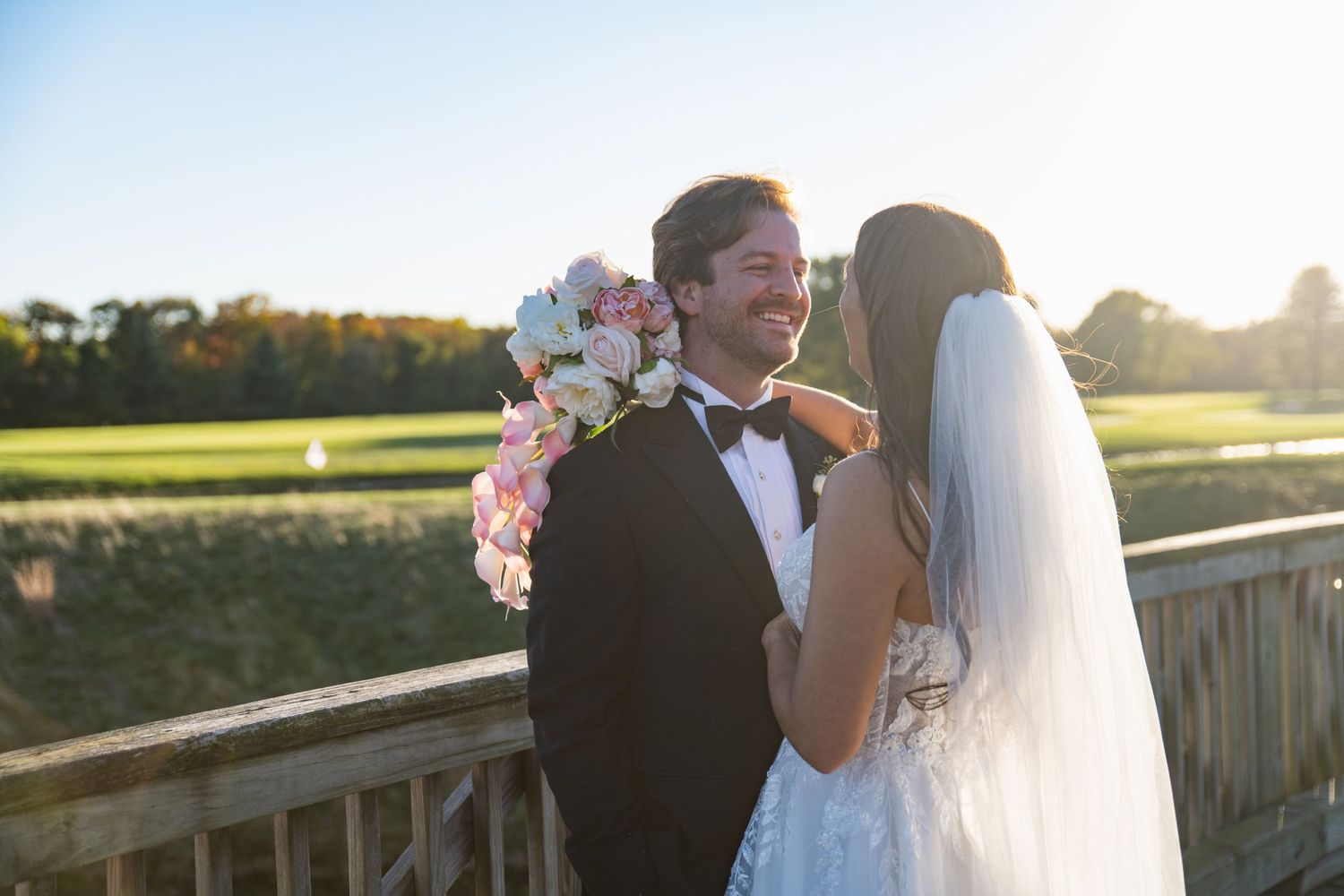 A romantic sunset wedding photo shoot on a wooden deck with pink floral decorations and golden hour lighting.