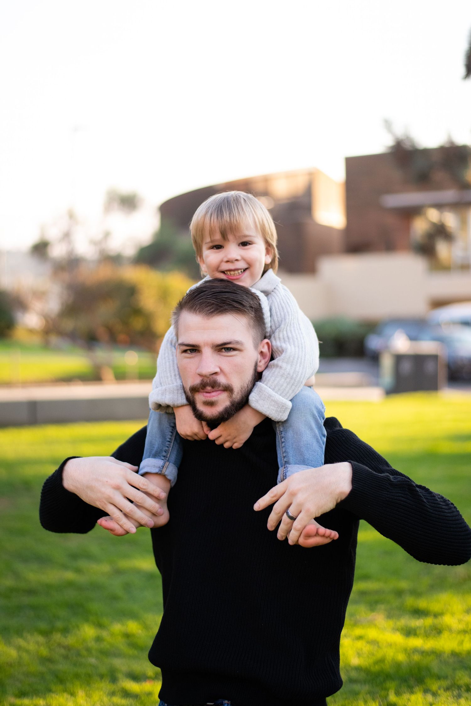 Playful father-child moment captured outdoors on grassy field during golden hour.