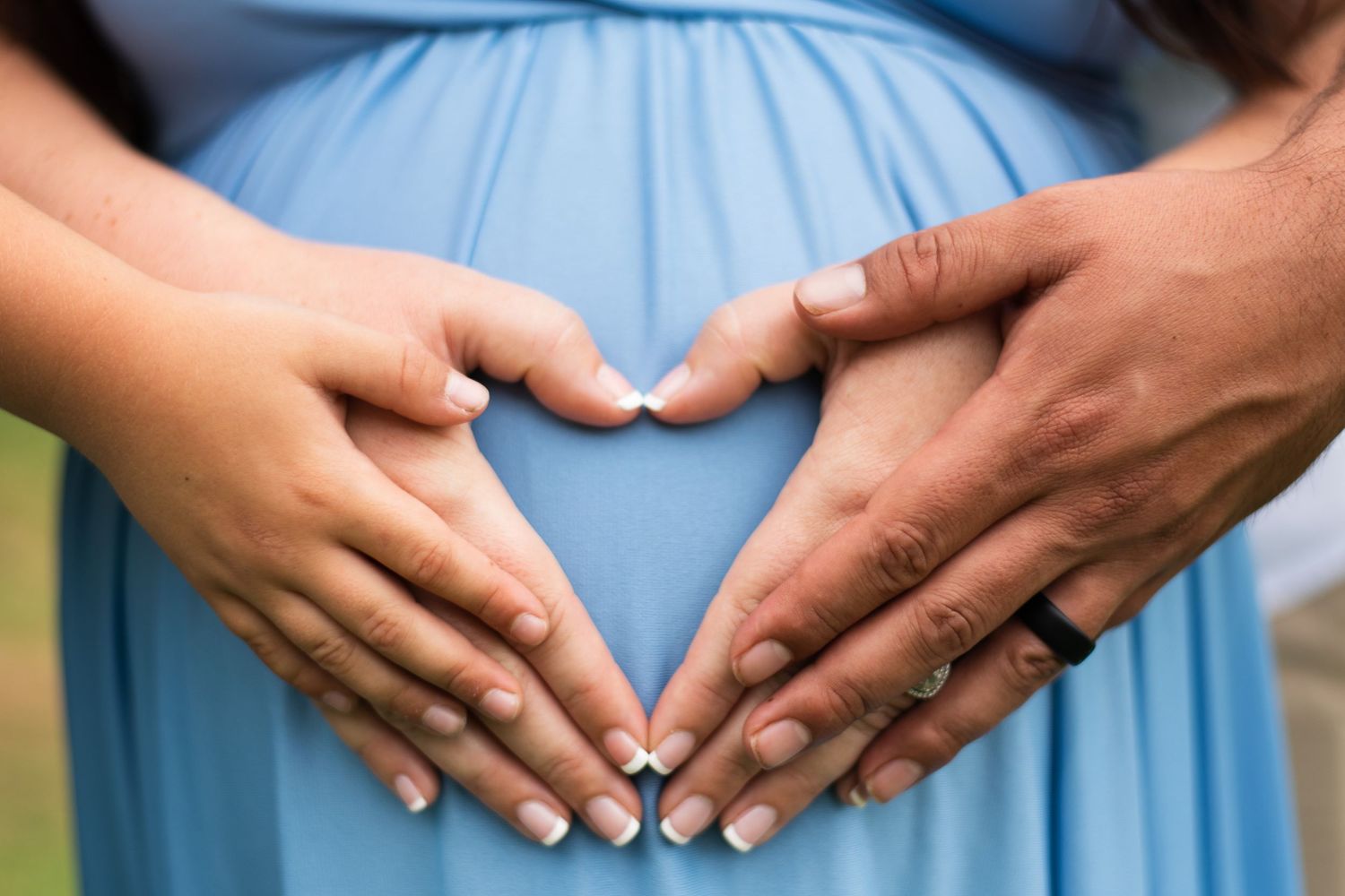 Close up of hands cradling a baby bump in a flowing blue maternity dress.