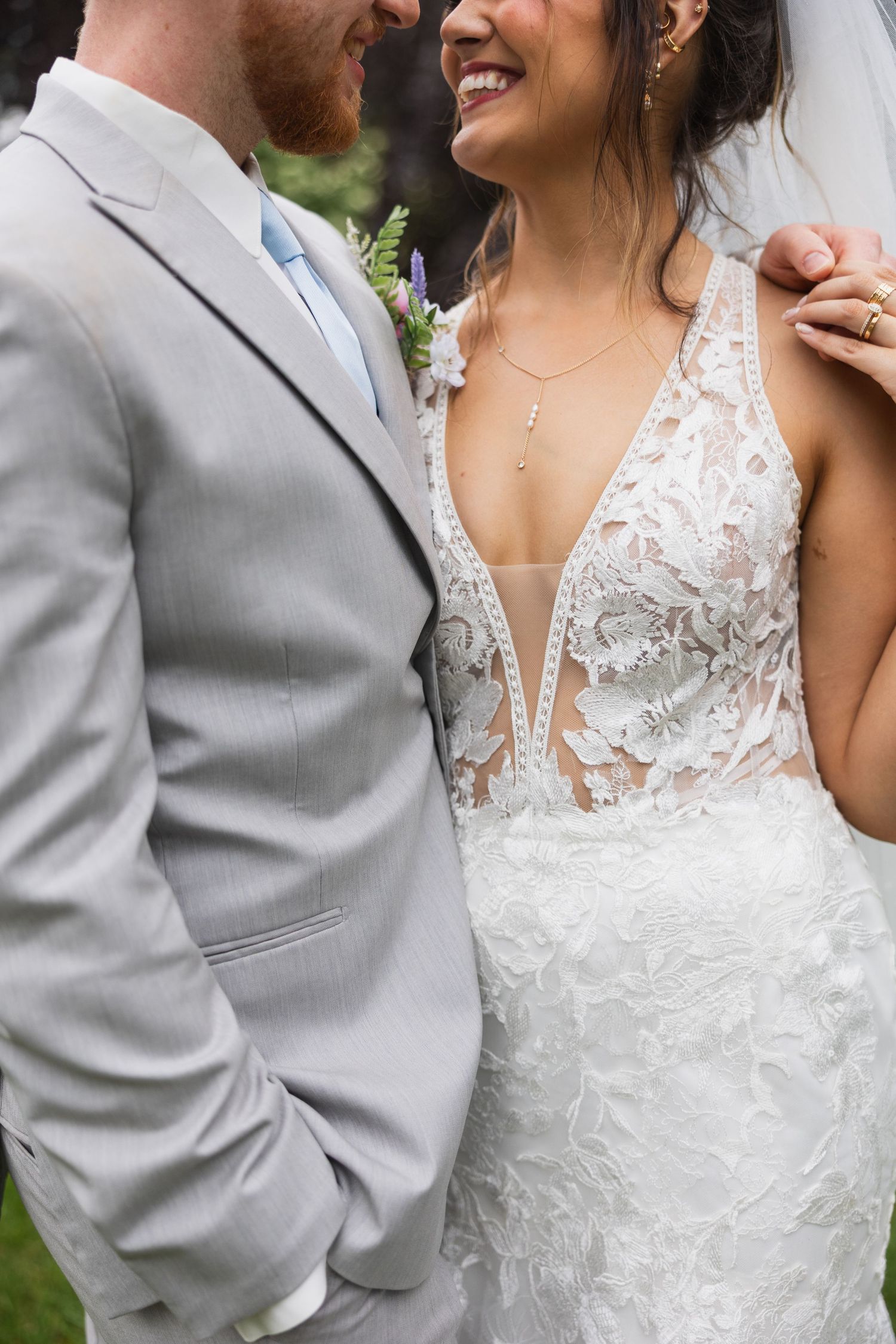 Close-up detail of white lace wedding dress against light gray suit.