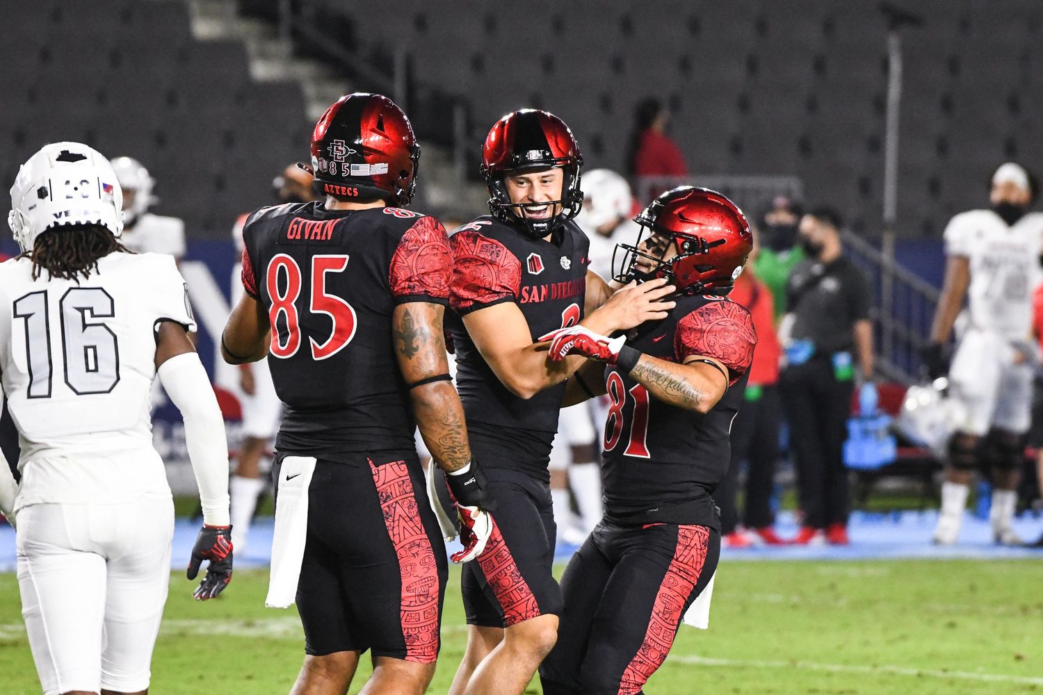 San Diego State football players in red uniforms celebrate on the field during a night game.