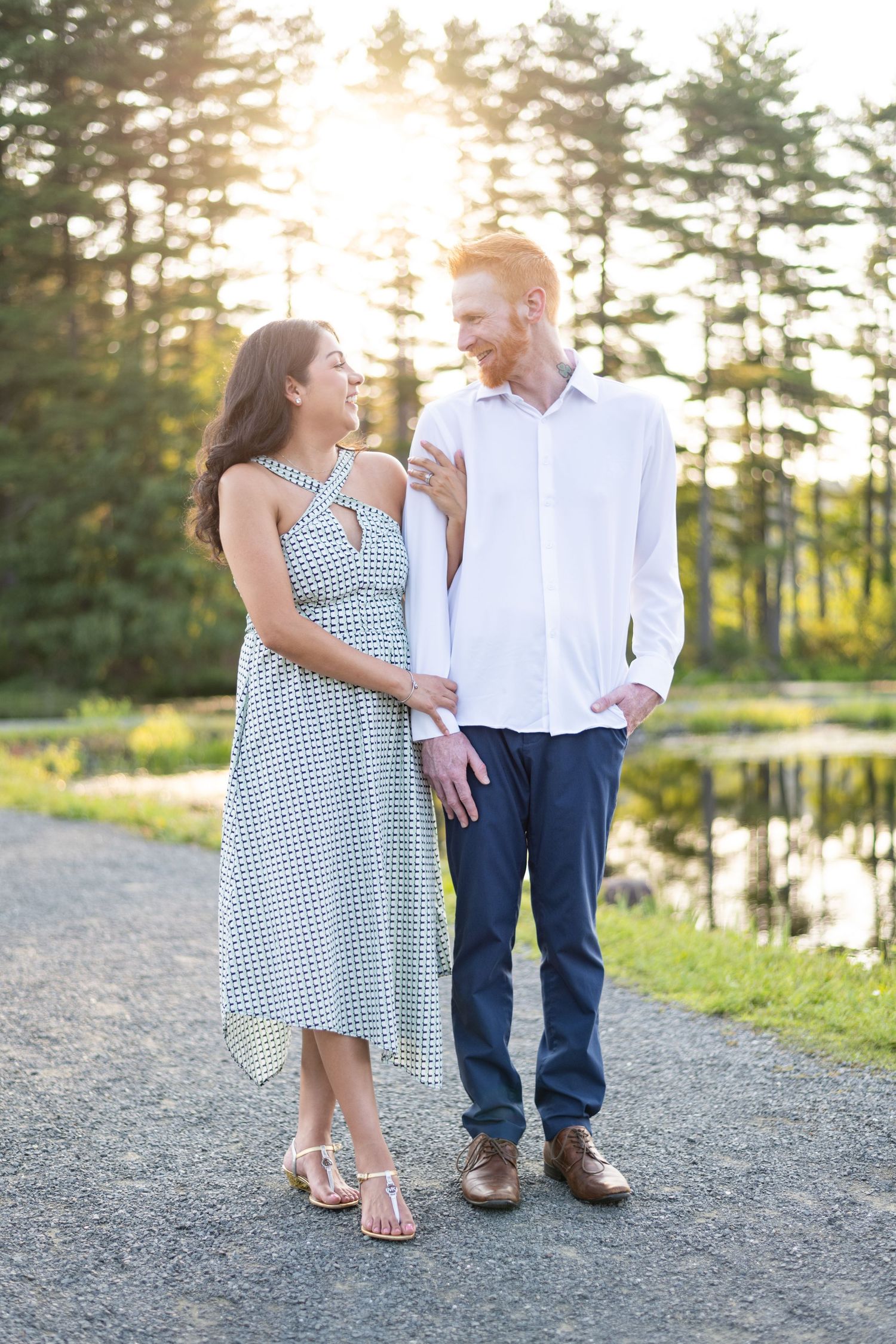 Couple shares tender moments at sunset by a lake while wearing casual summer outfits.