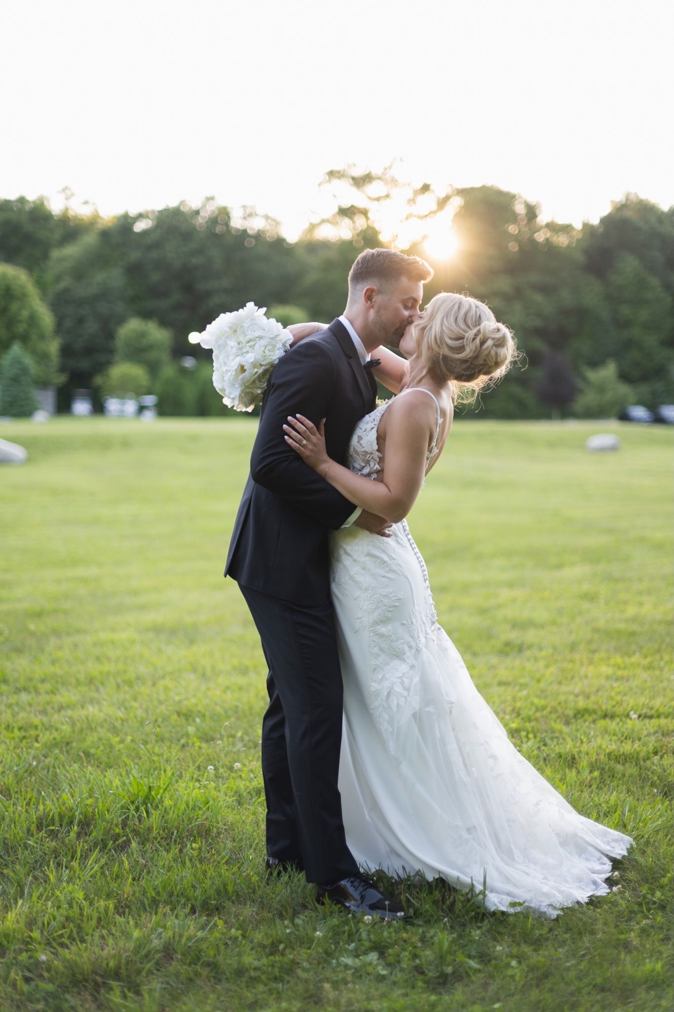 A romantic sunset wedding portrait with the couple embracing on a grassy field.