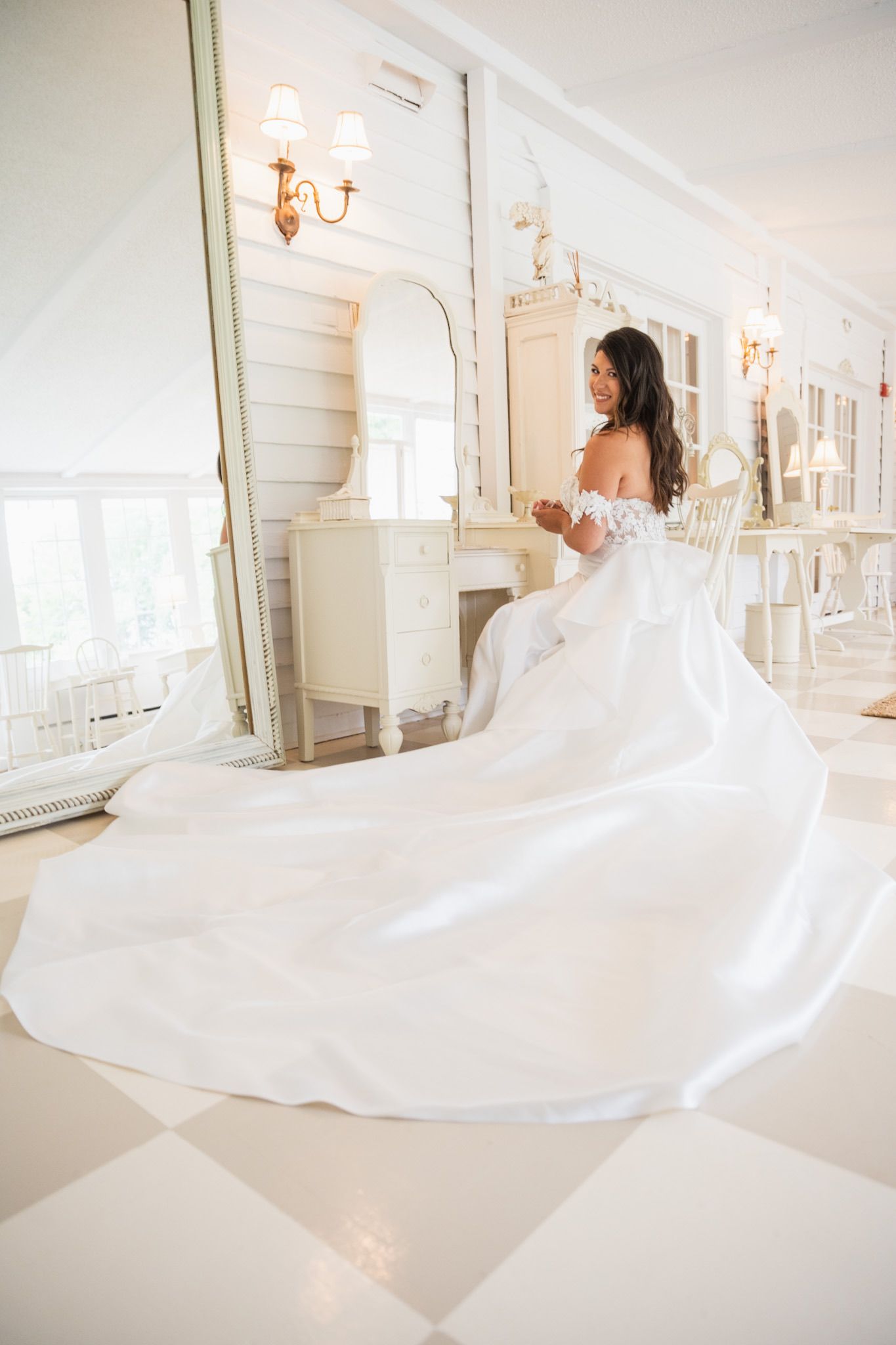 Wedding dress with dramatic long train flowing across white floor in bright indoor setting with chandeliers.