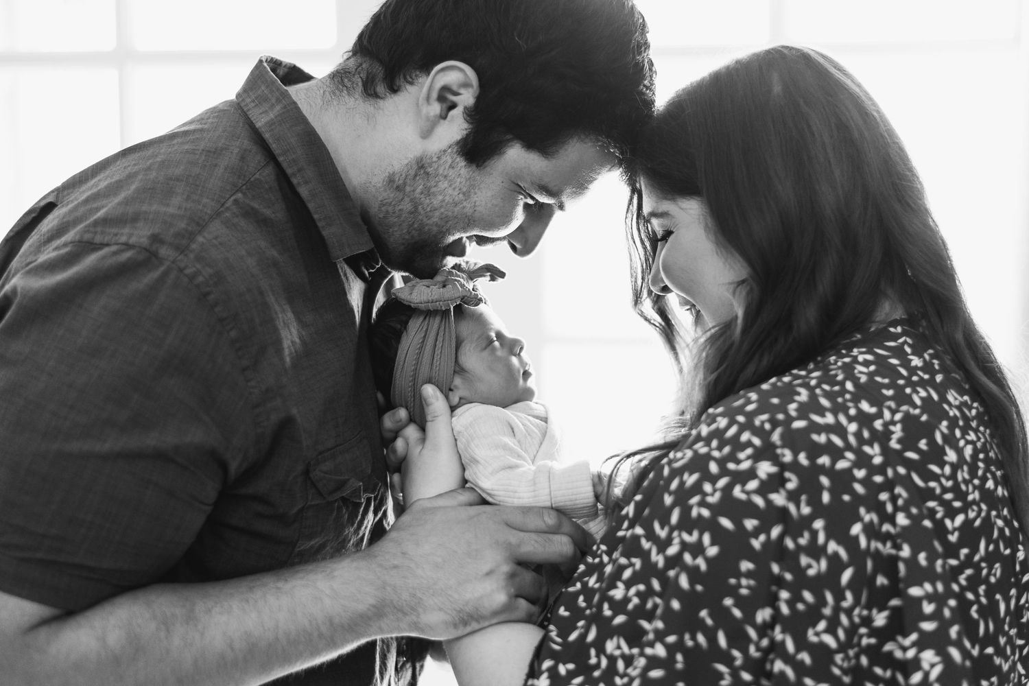 Black and white intimate portrait of couple sharing tender moment with newborn baby.
