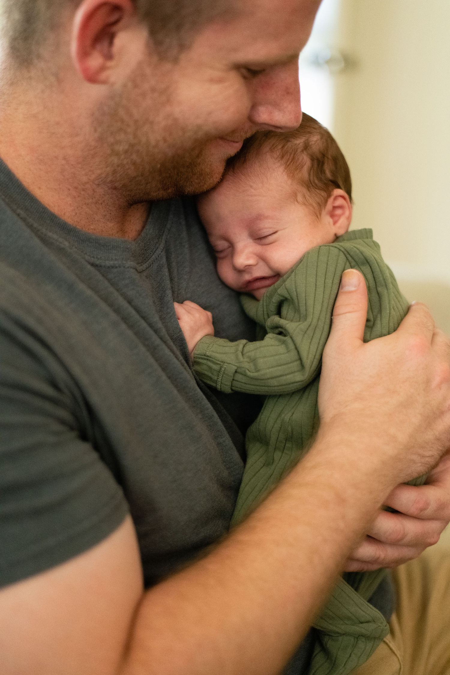 Intimate nurturing moment between parent and infant wearing green on beige background.