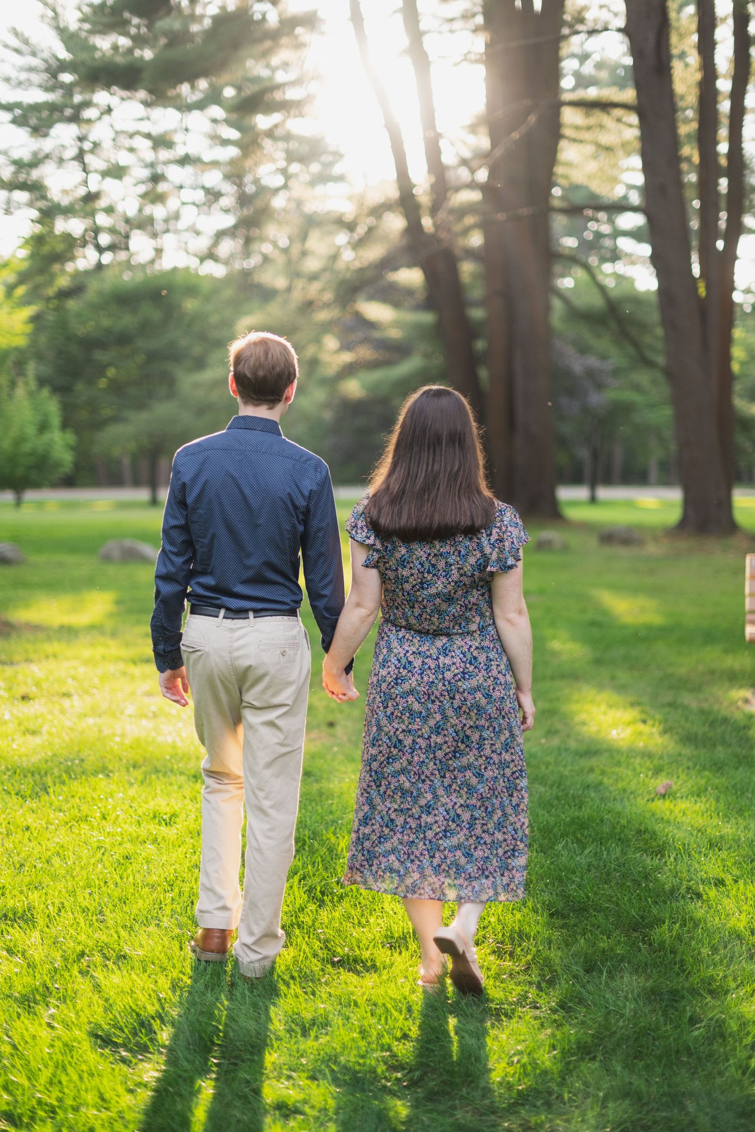 Couple walks hand in hand through a sunlit forest path during golden hour.