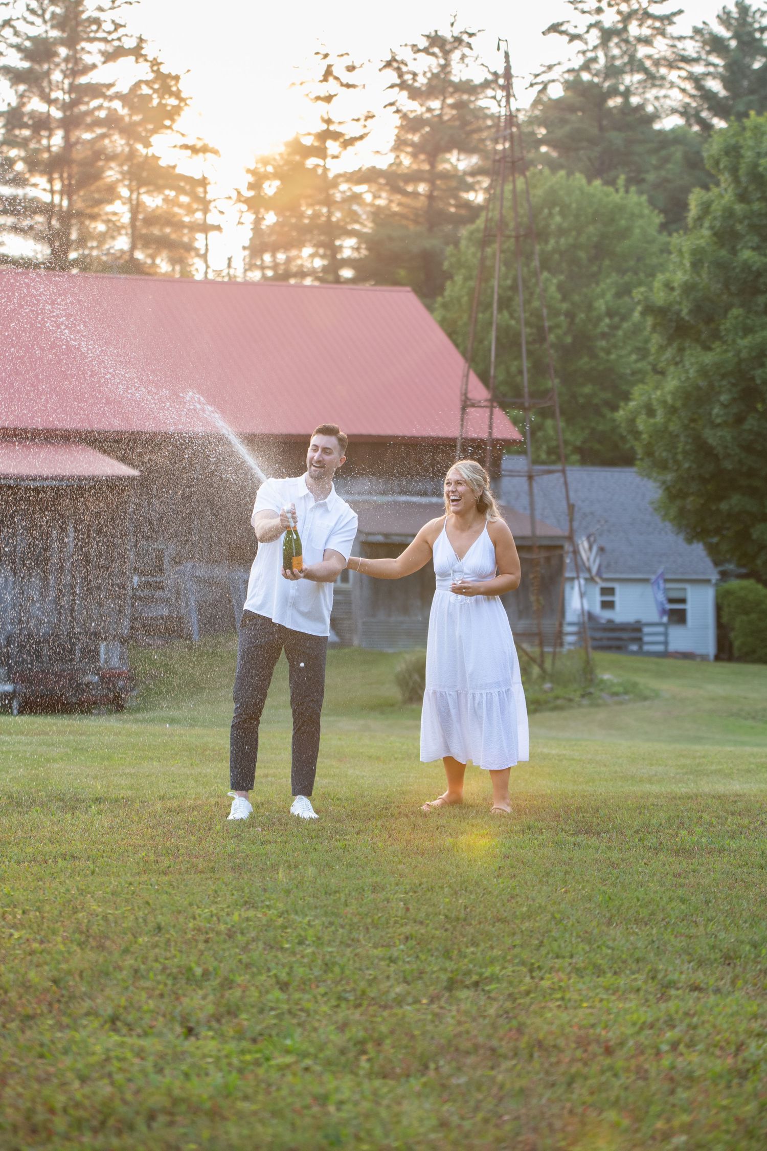 Playful couple spraying water during sunset photo session near rustic cabins.