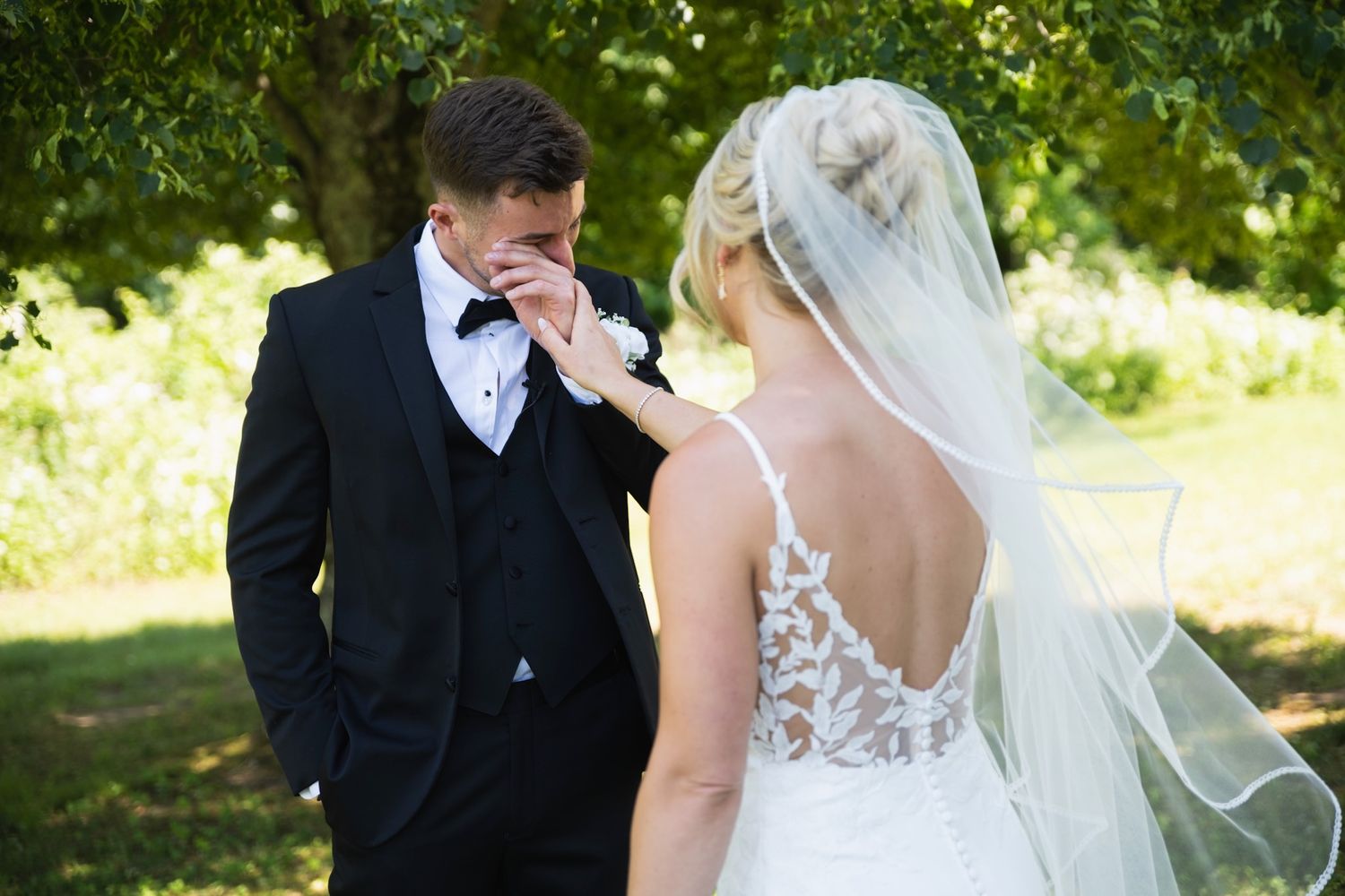 Couple sharing an emotional first look moment in a sunny outdoor garden setting.