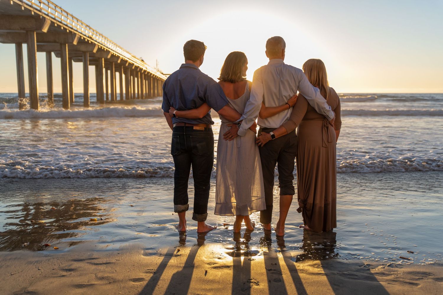Group stands together watching sunset at beach pier.