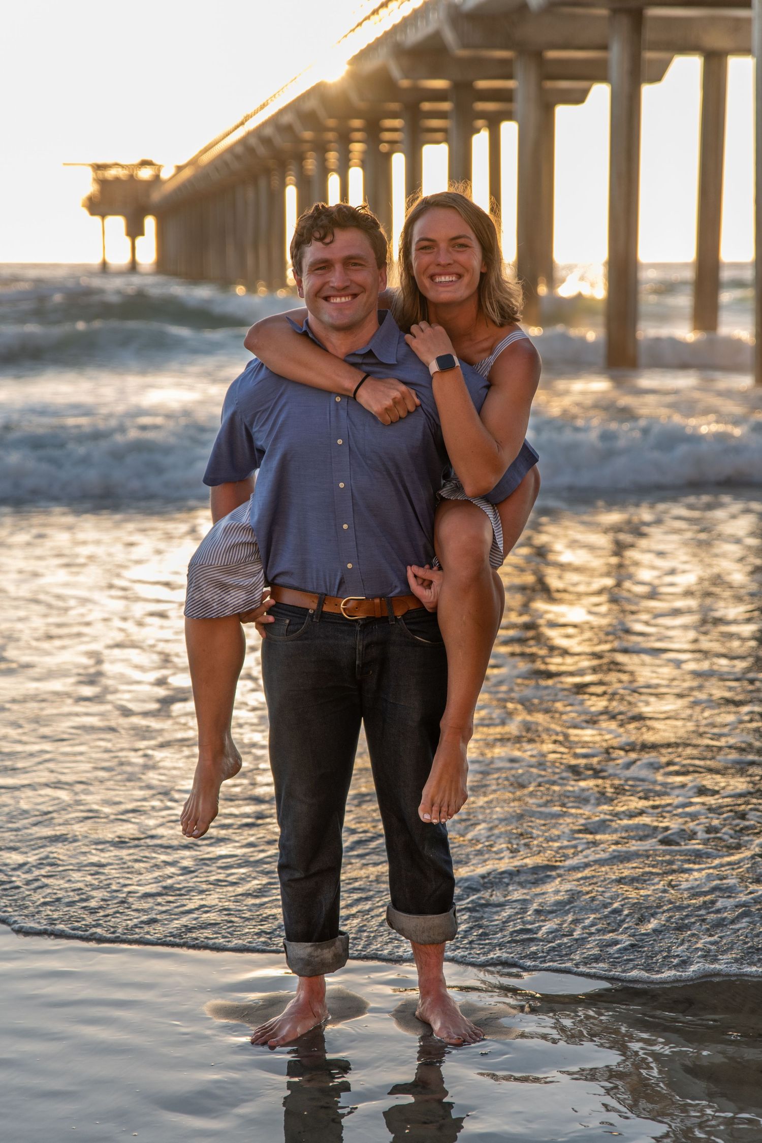 Couple shares a romantic moment at sunset by a beach pier.