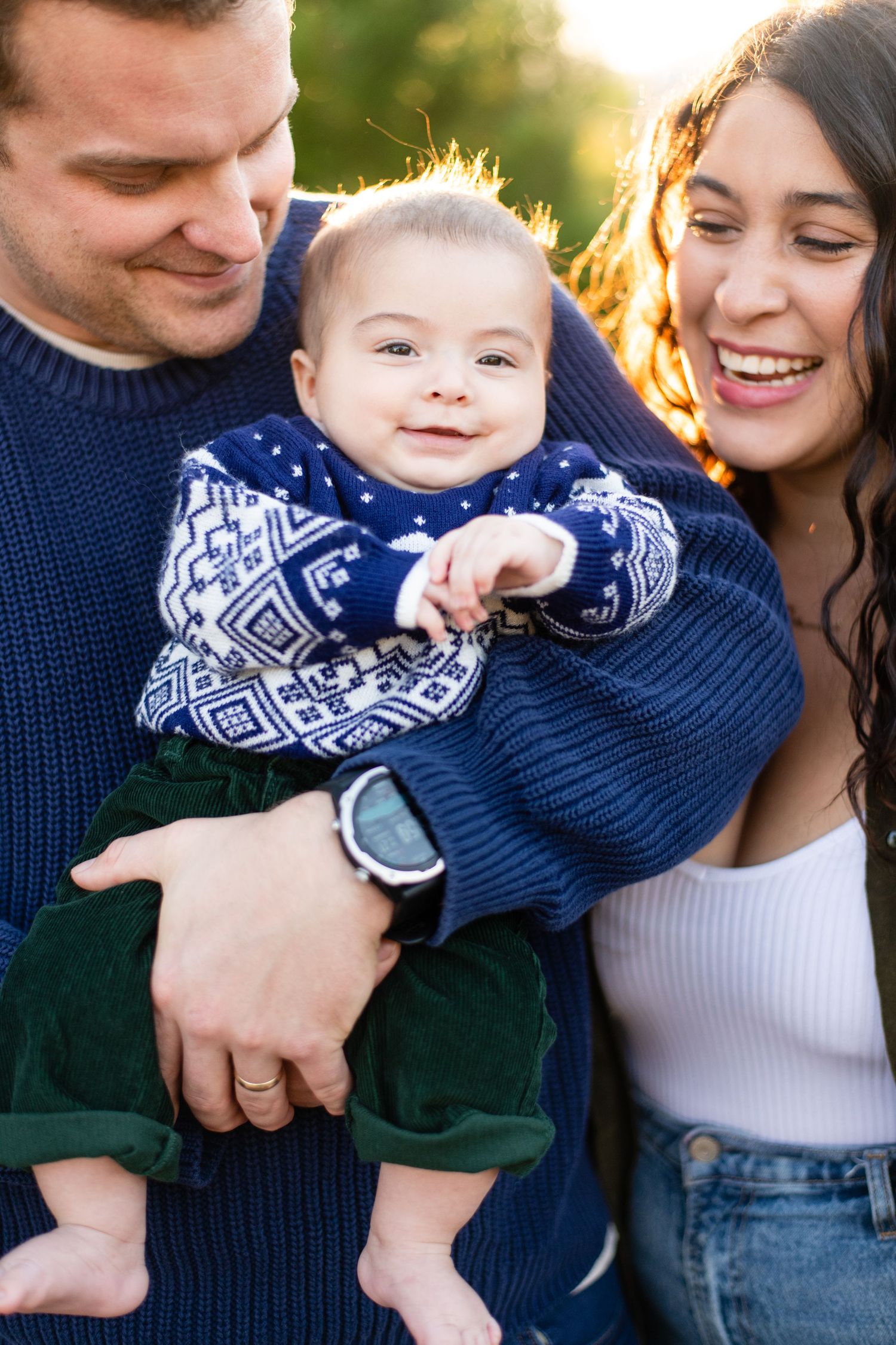 Family cuddles and shares laughs while wearing cozy winter sweaters outdoors.