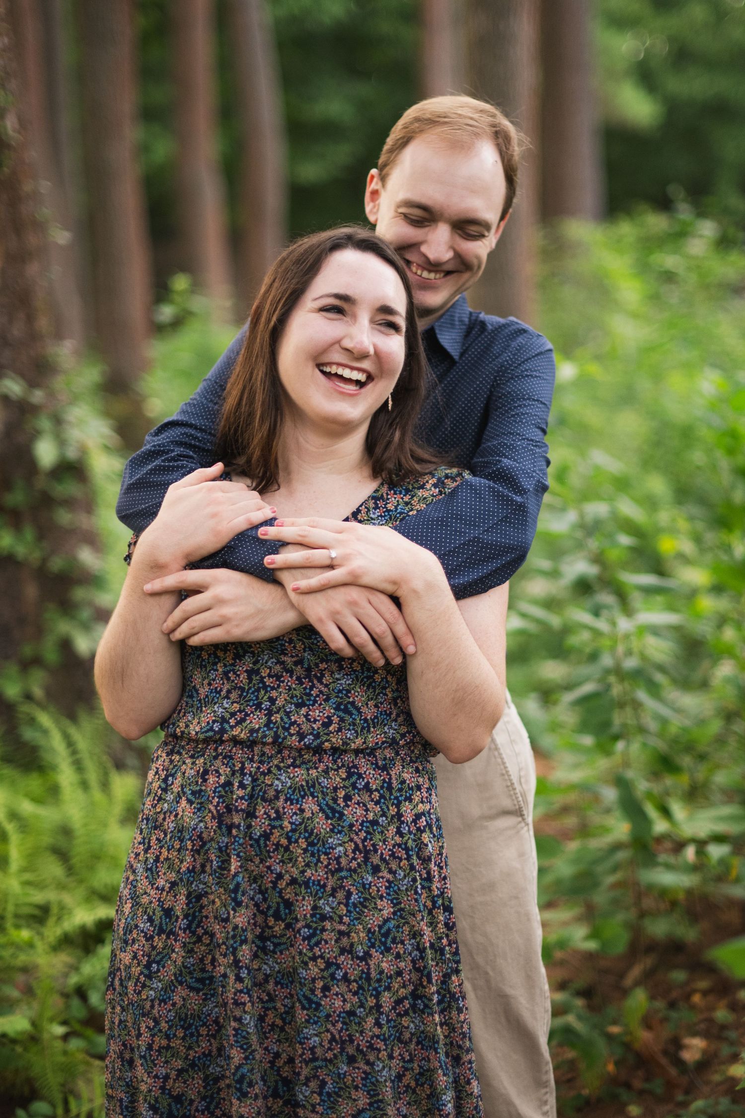 A couple embraces while surrounded by lush green forest during an outdoor photoshoot.
