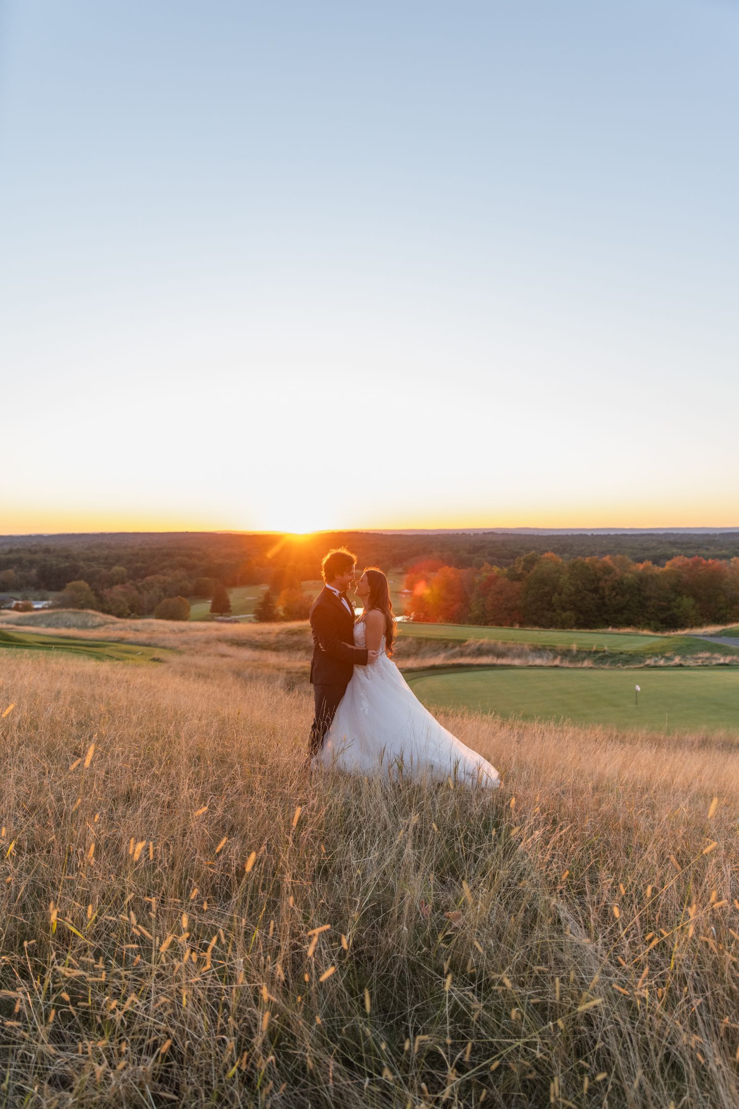 A couple sits in a golden wheat field at sunset as warm light illuminates the romantic countryside scene.