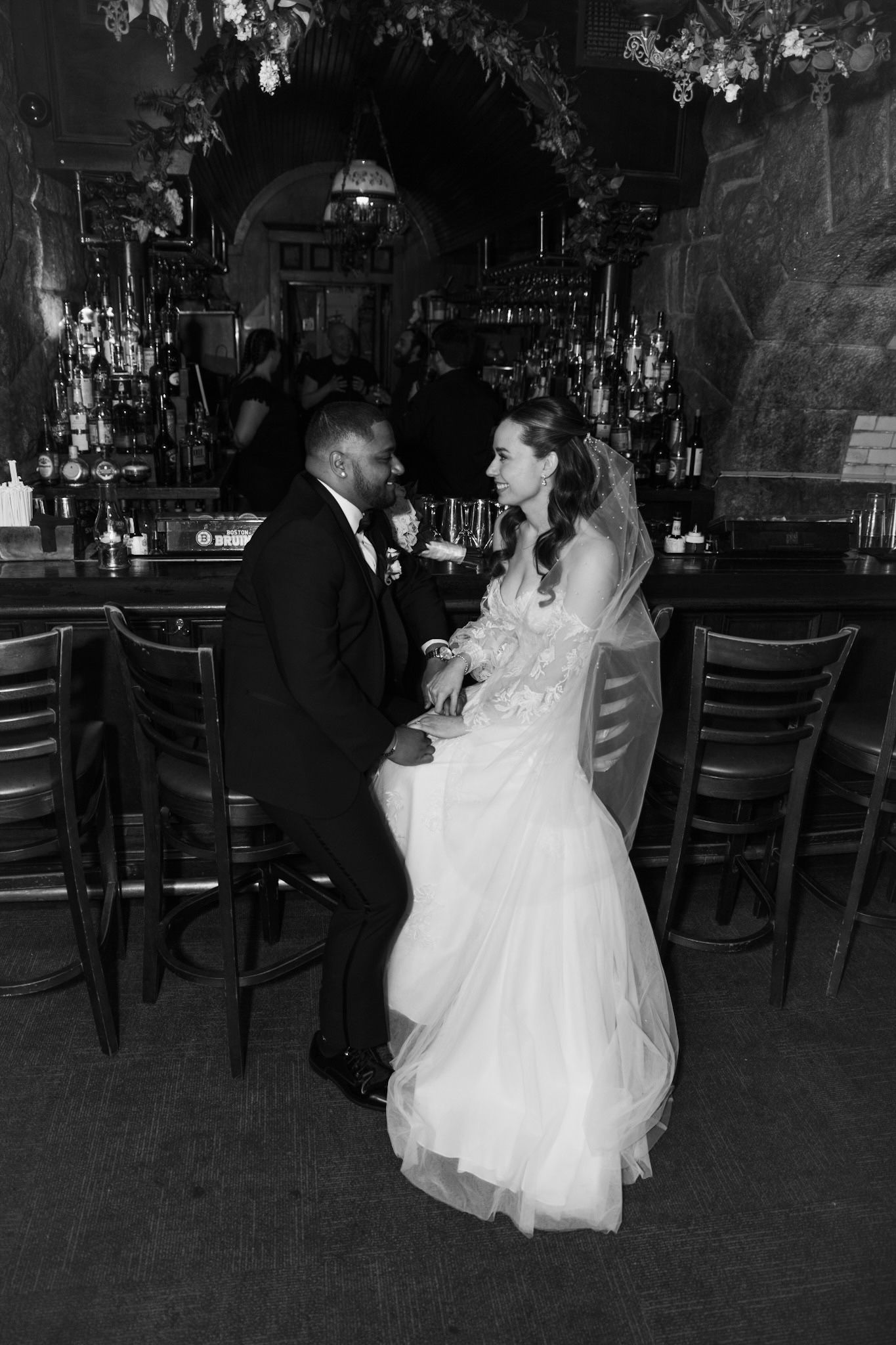 Couple sharing an intimate moment in front of a dimly lit bar with chandeliers overhead.