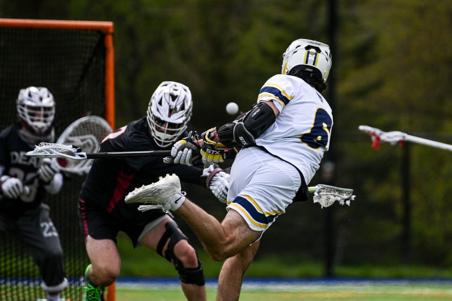 Two lacrosse players battle for the ball in front of the goal during an intense outdoor game.