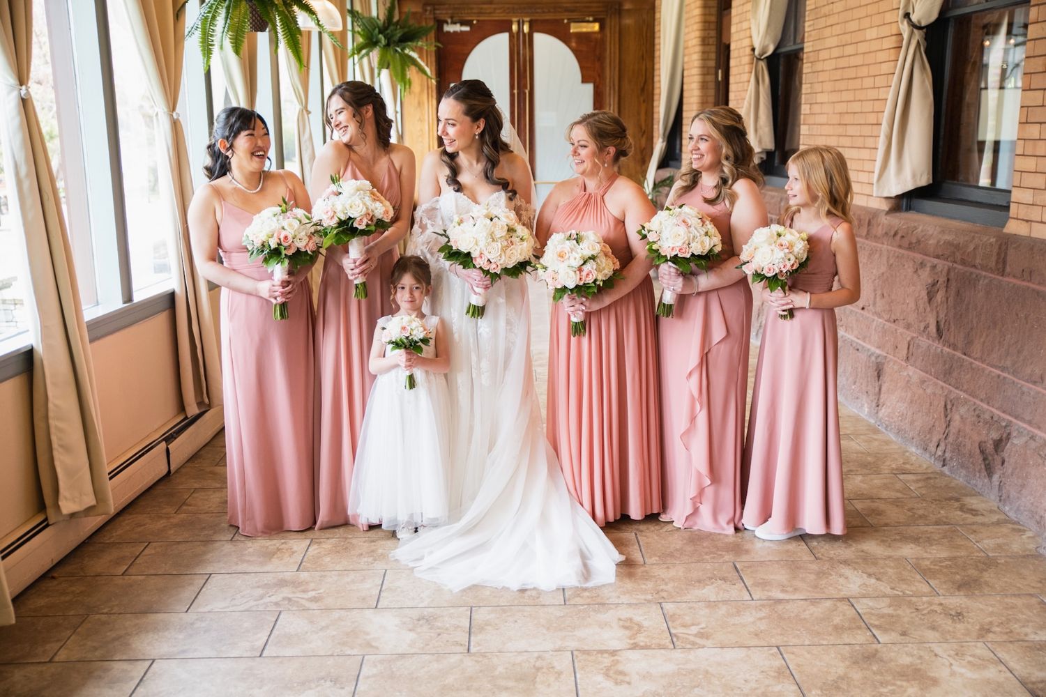 Bridesmaids in coral pink dresses pose with the bride in an elegant indoor venue setting.