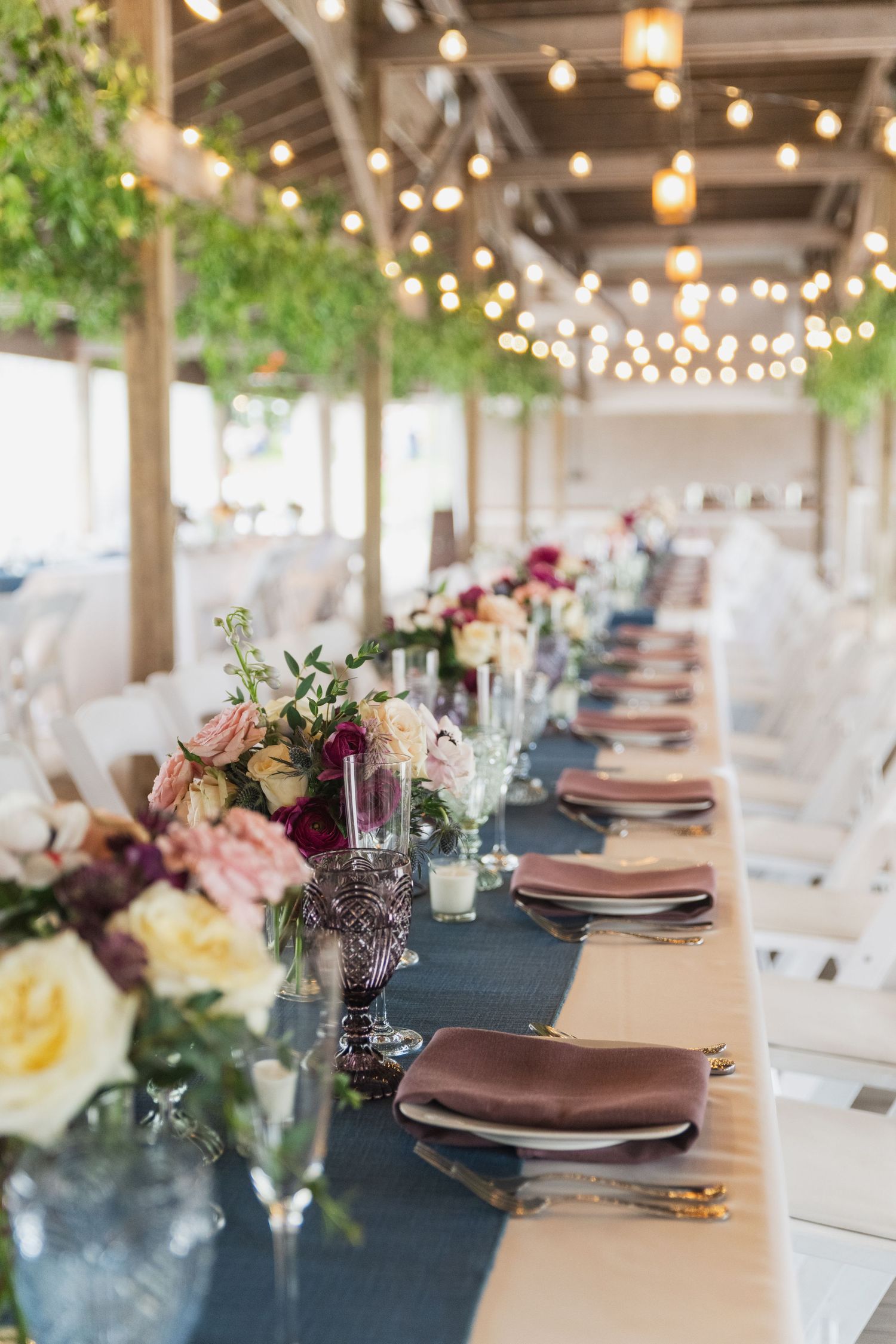 Elegant wedding reception table setting with string lights and floral centerpieces.