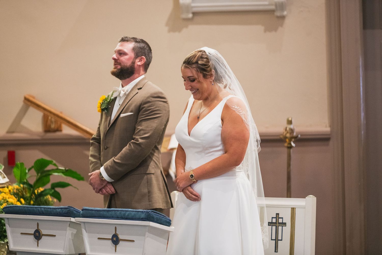 Wedding ceremony underway in a church with white walls and sunlit windows.