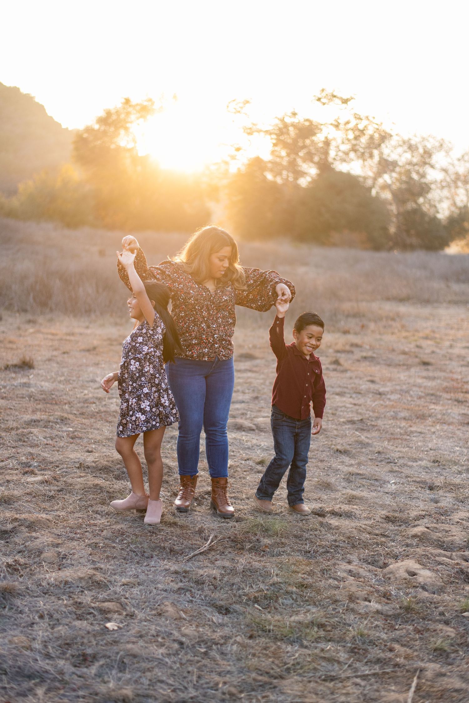 Family dancing together in a field at golden hour with joyful expressions.
