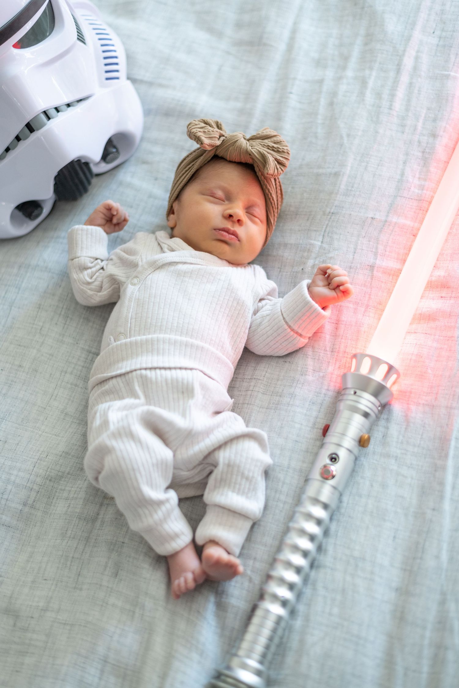 Baby sleeps near Star Wars themed lightsaber and Stormtrooper helmet.