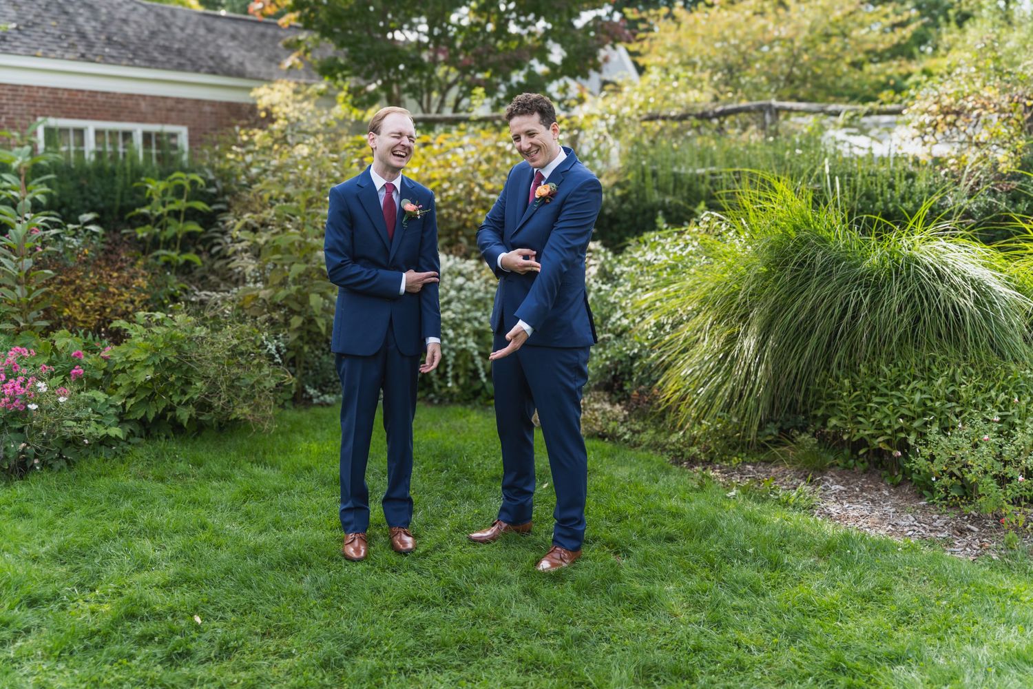 Two people in navy suits share a joyful moment while standing in a lush garden setting.