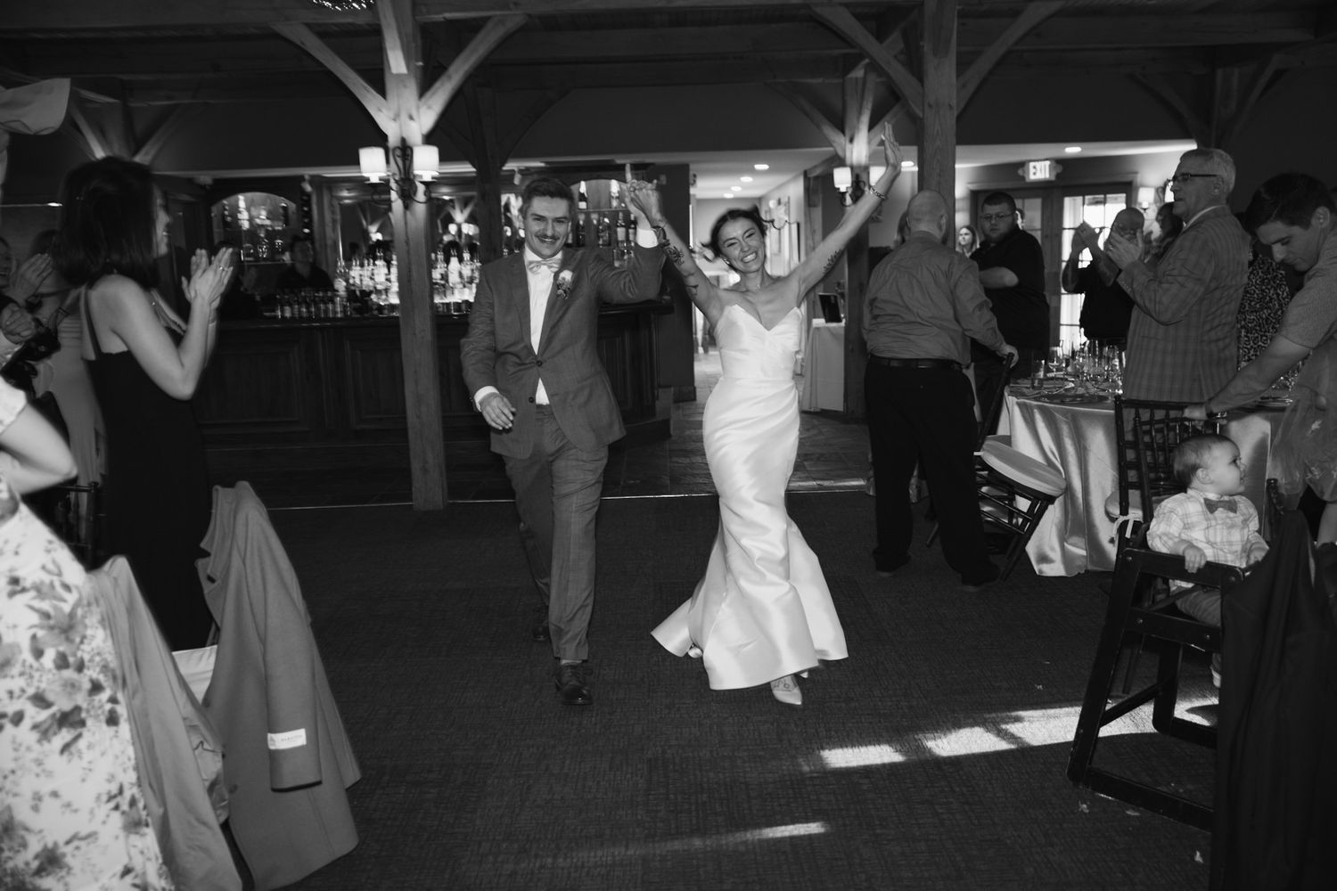A joyful moment captured in black and white as wedding guests dance at an indoor reception.