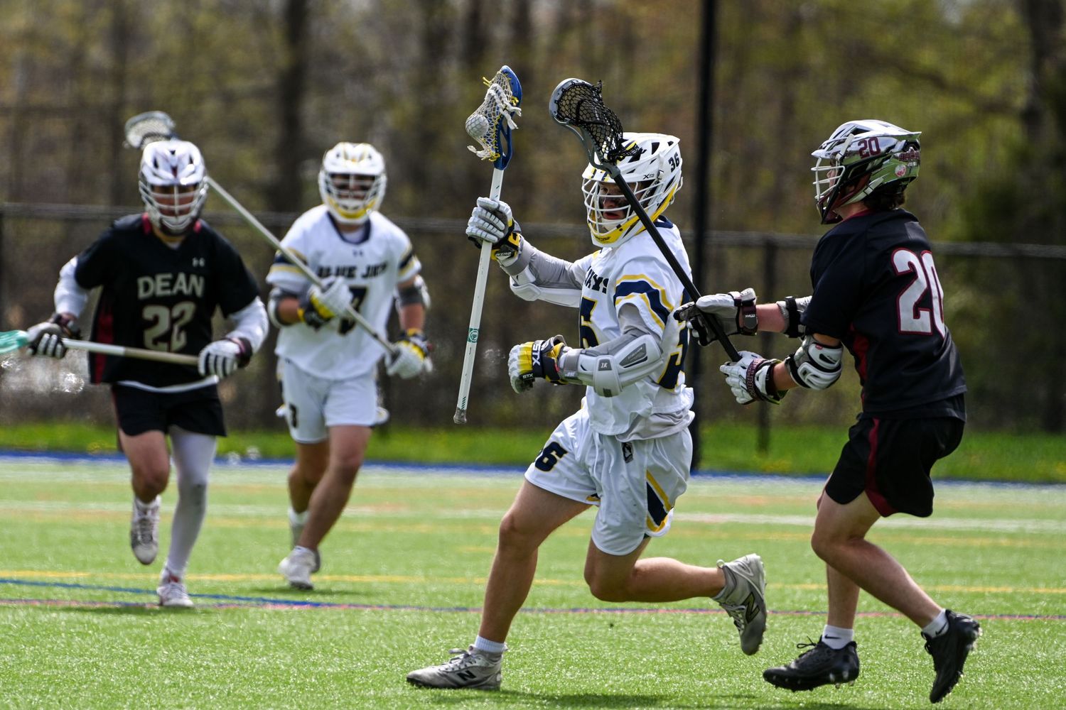 A lacrosse player in white uniform dodges defenders during an outdoor collegiate lacrosse game.