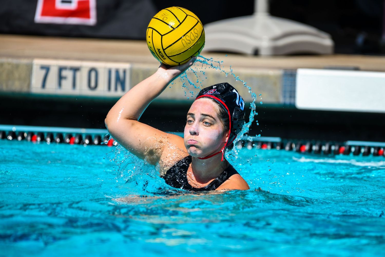 A water polo player in dark uniform prepares to throw the ball during a pool match.