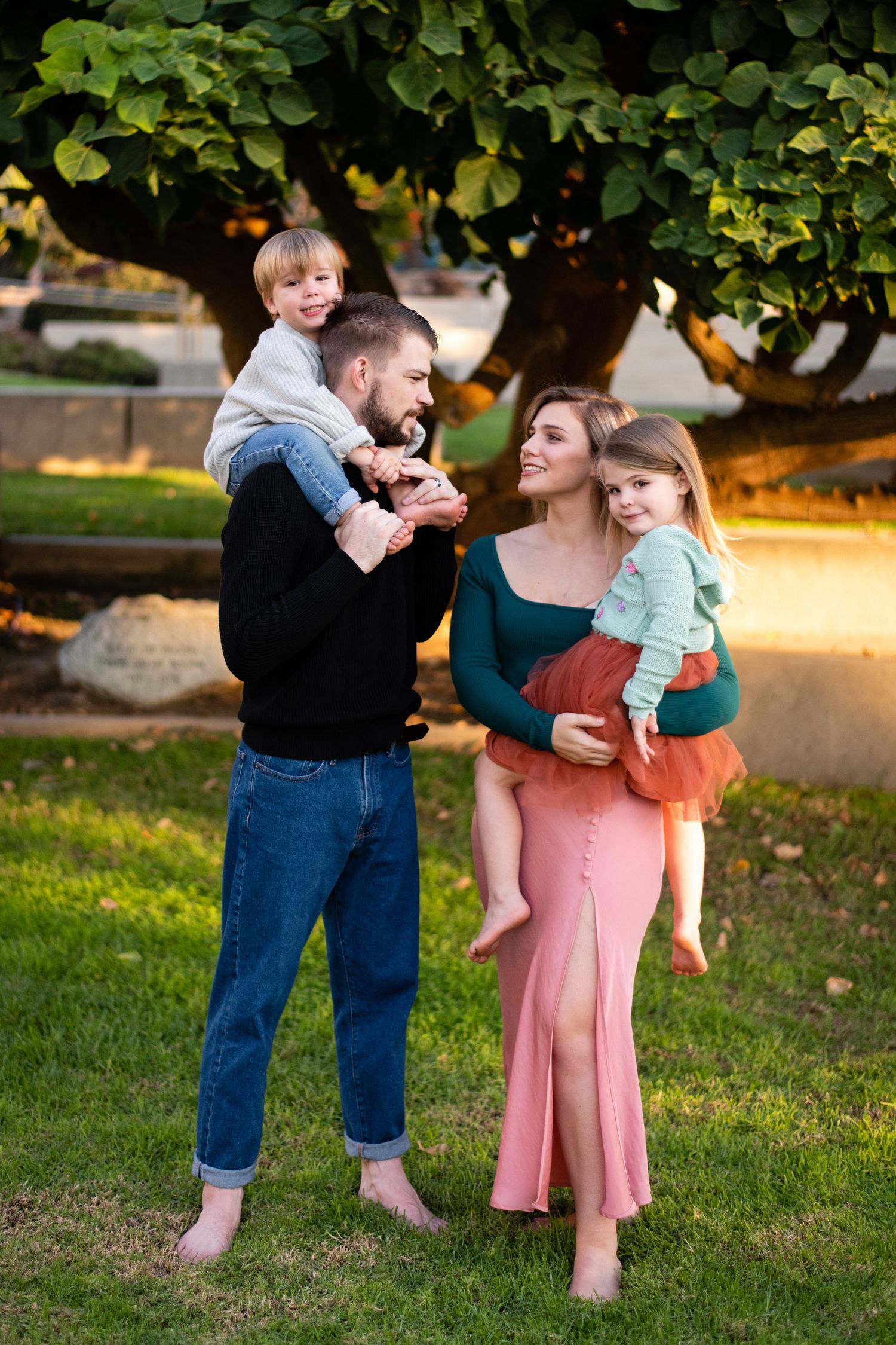 Family enjoying a playful moment together under a tree in a park during sunset.
