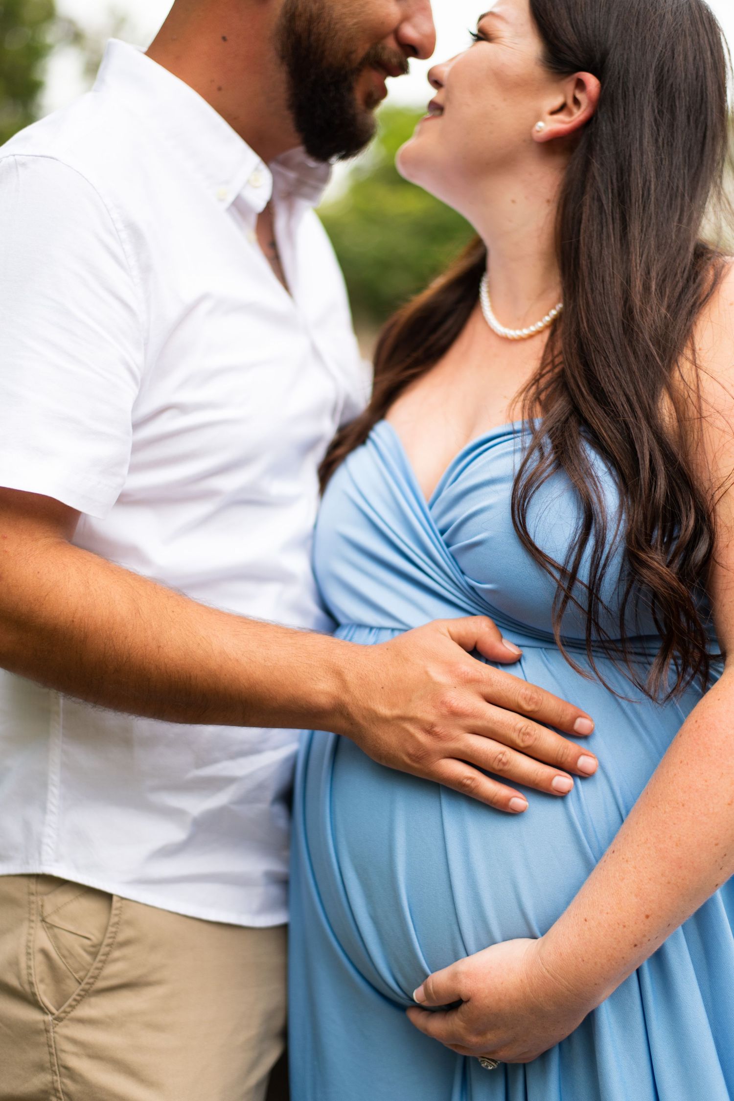 Intimate maternity photoshoot with couple in white shirt and light blue dress outdoors.
