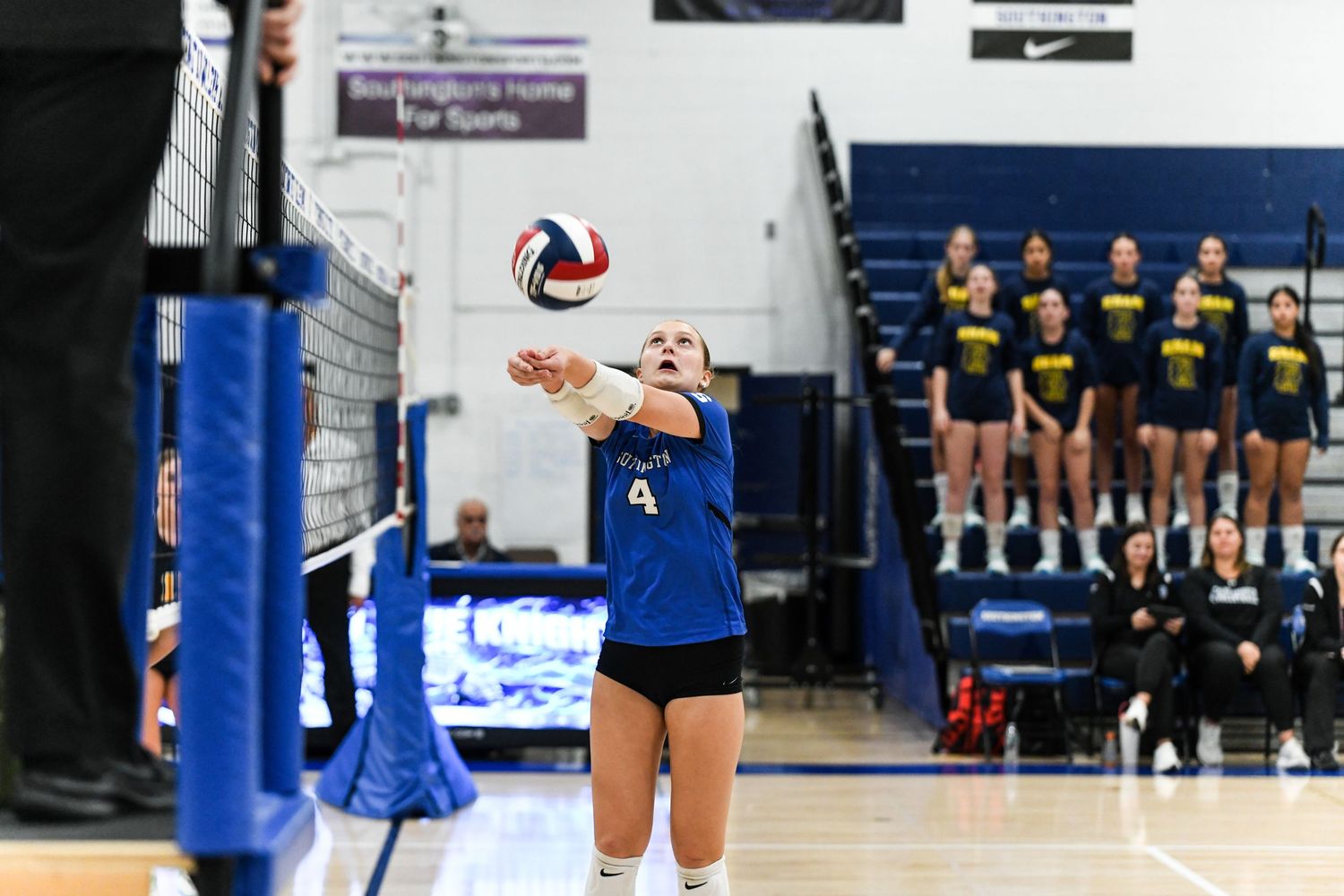 Female volleyball player in blue uniform bumping the ball during an indoor high school volleyball match.