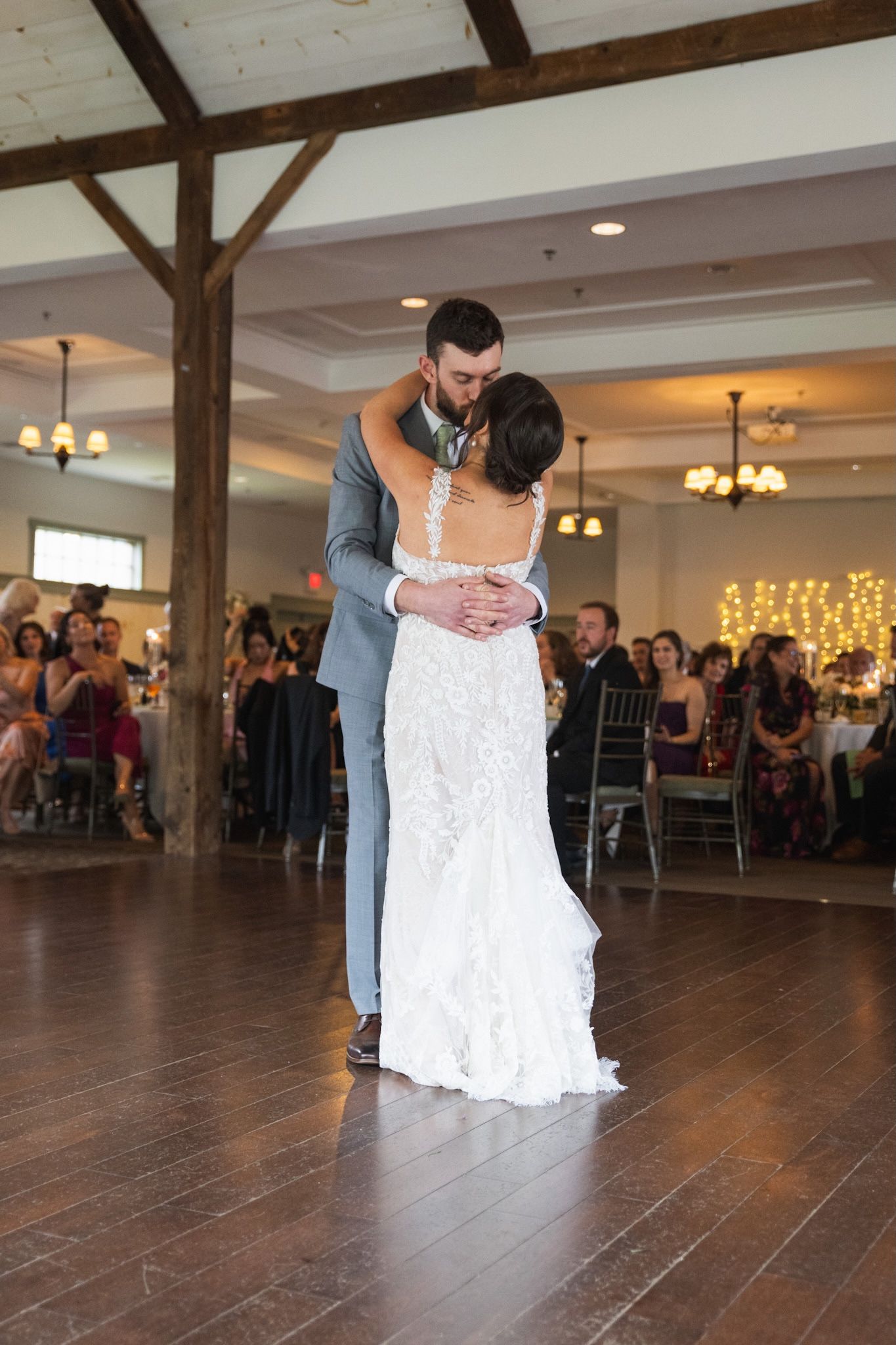Couple dancing on rustic wooden floor beneath exposed ceiling beams.
