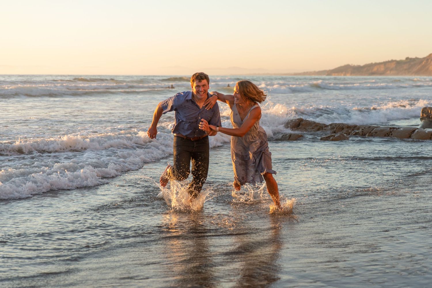 Playful moment at sunset as people splash through ocean waves along a beach.