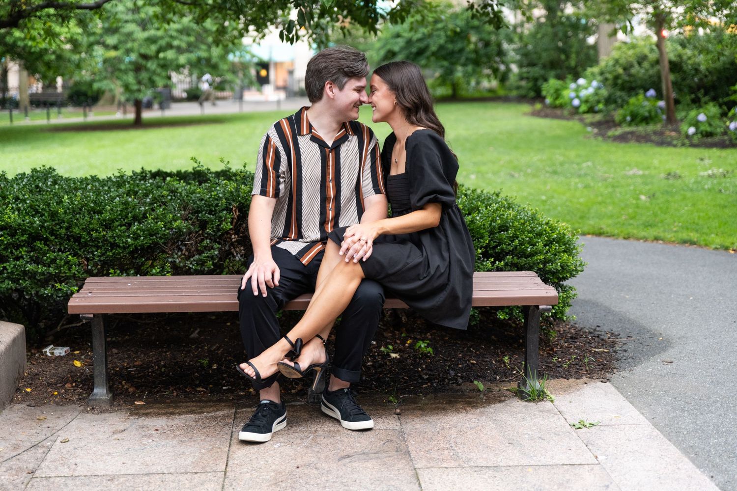 Romantic couple sitting together on a park bench surrounded by greenery and walking paths.