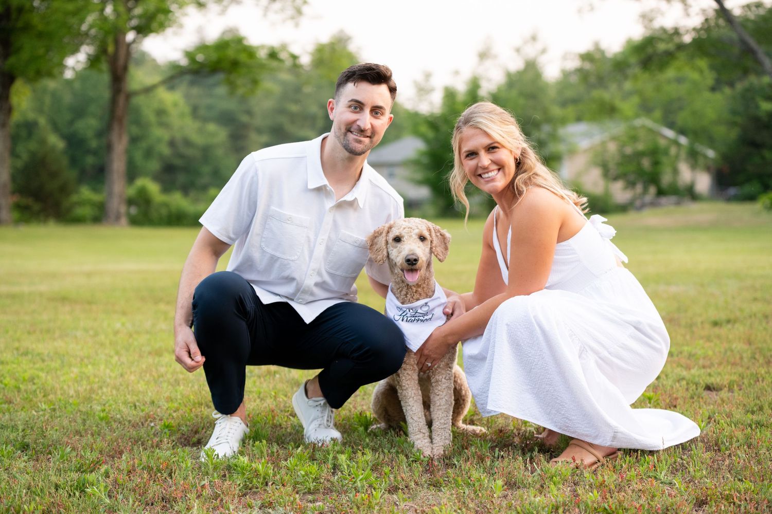 A couple sits on grassy lawn with their golden retriever during an outdoor photoshoot.