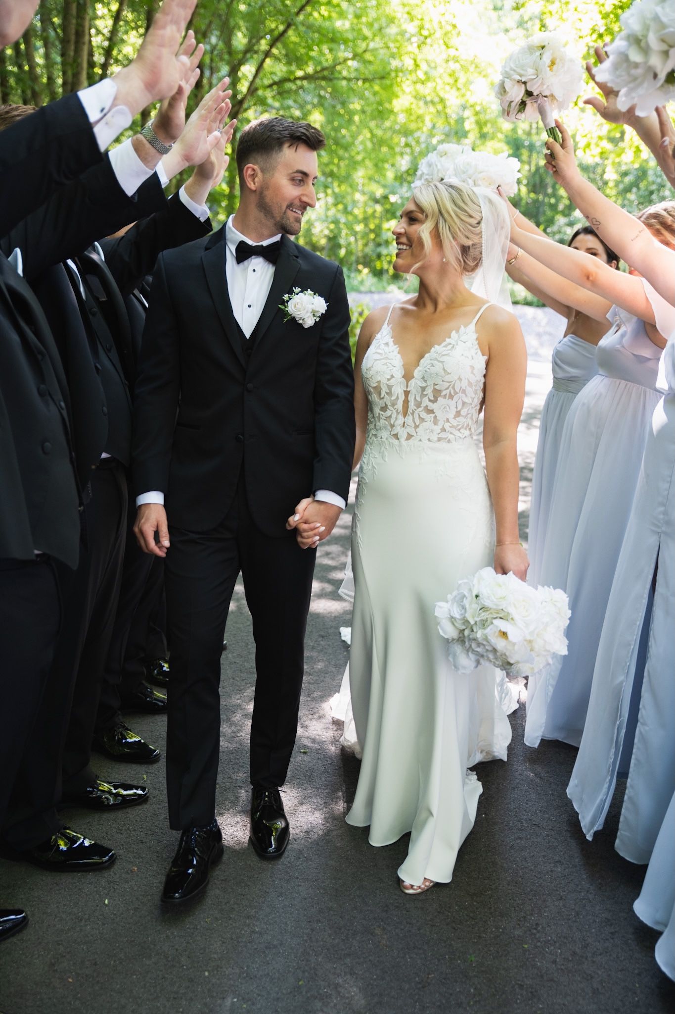 Wedding party in black tuxedos and light colored dresses lined up for formal photos.