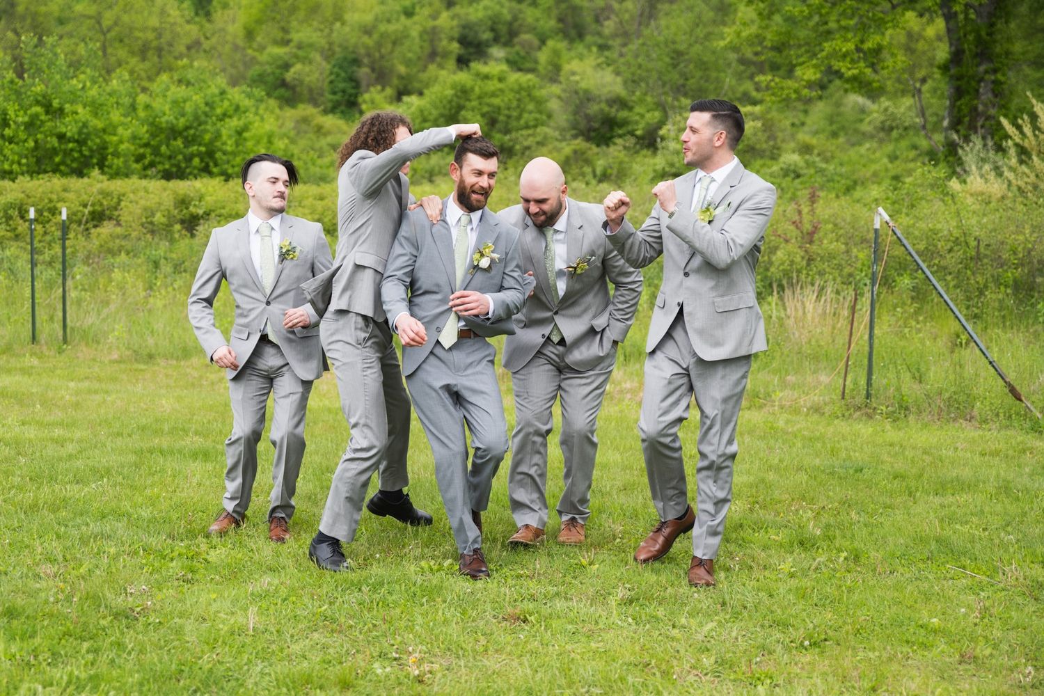 Groomsmen in light gray suits pose playfully outdoors on wedding day.