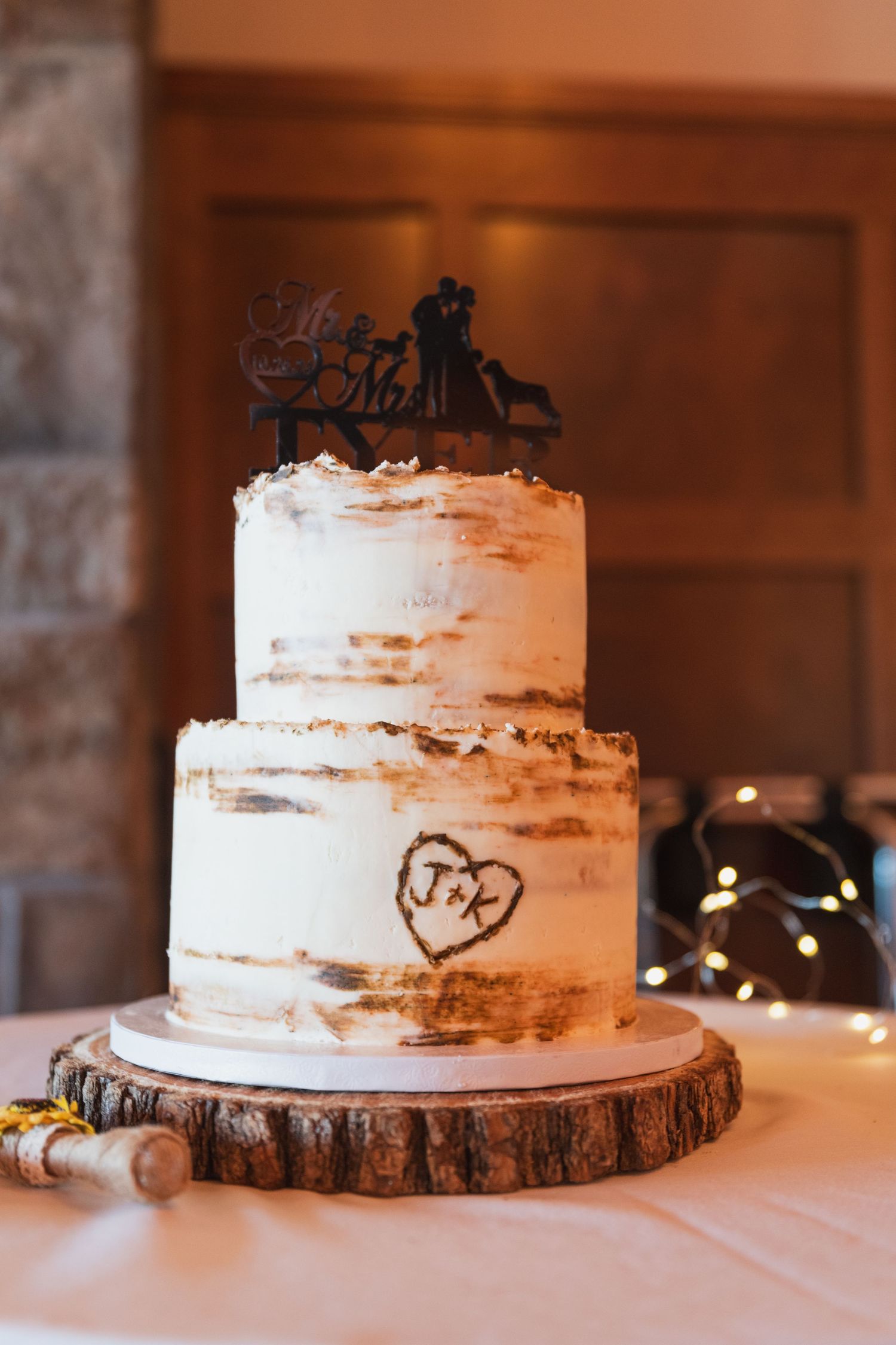 Rustic white wedding cake displayed on wooden slice with carved heart detail.