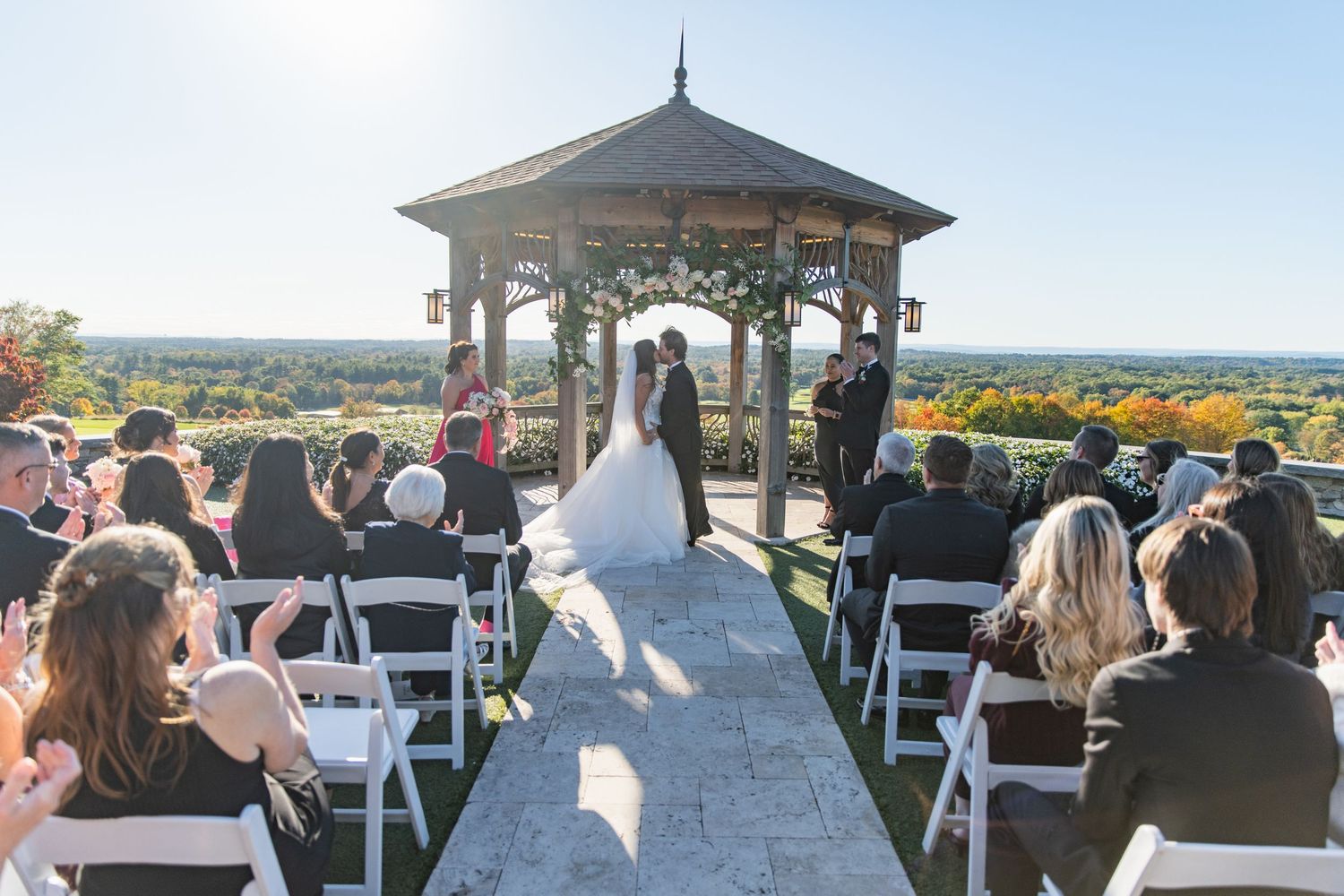 Panoramic view of an outdoor wedding ceremony setup with white chairs and gazebo overlooking scenic mountains.